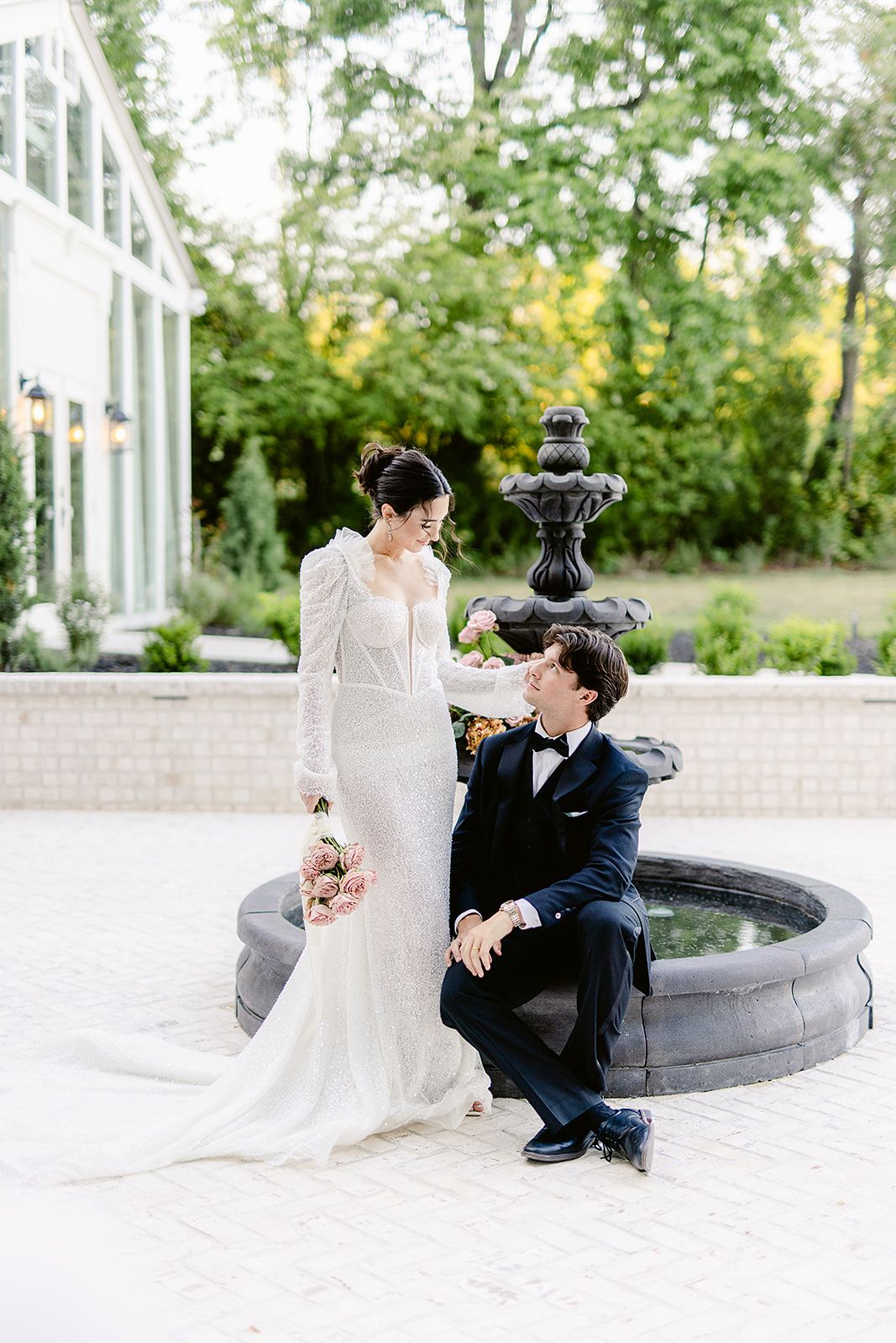 Romantic wedding couple shares tender moments by a stone fountain in an elegant garden setting.
