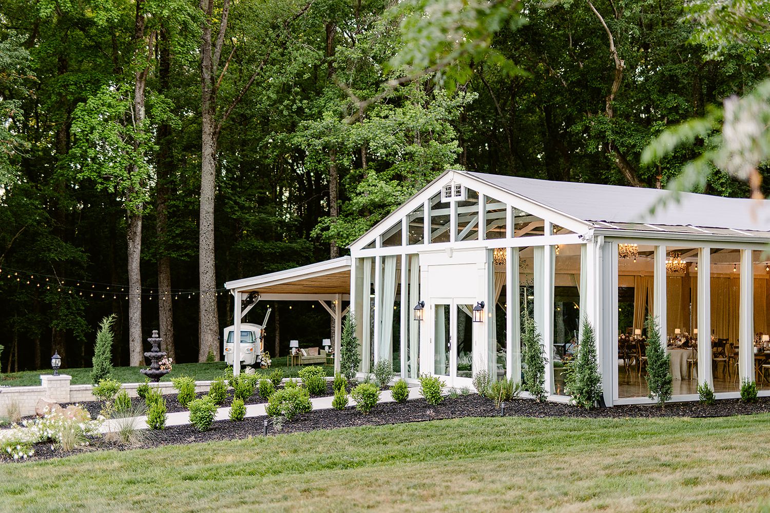 A row of white wedding venue buildings nestled among green trees and landscaping.