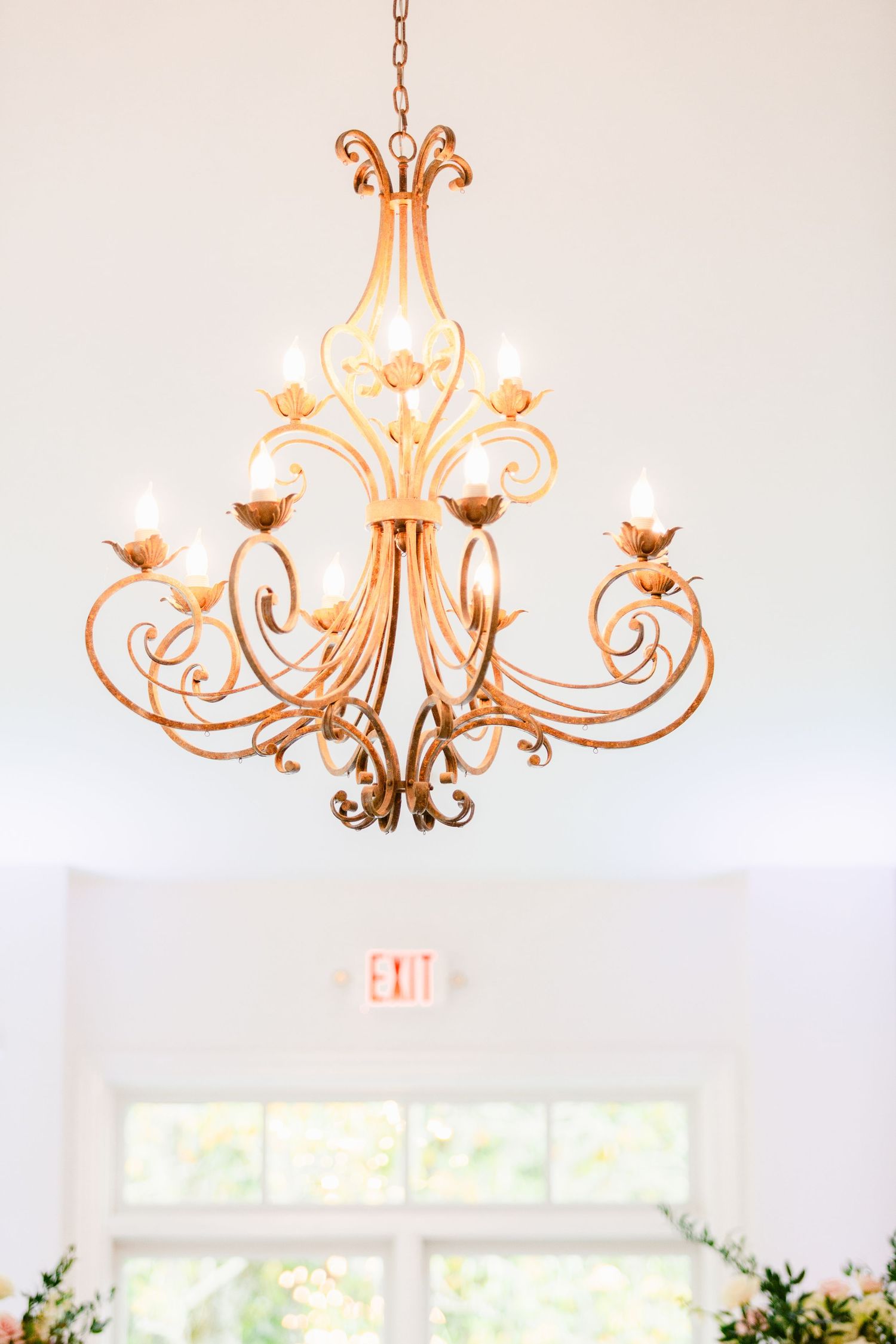 Elegant gold chandelier with ornate scrollwork and floral details hangs in a bright white room.