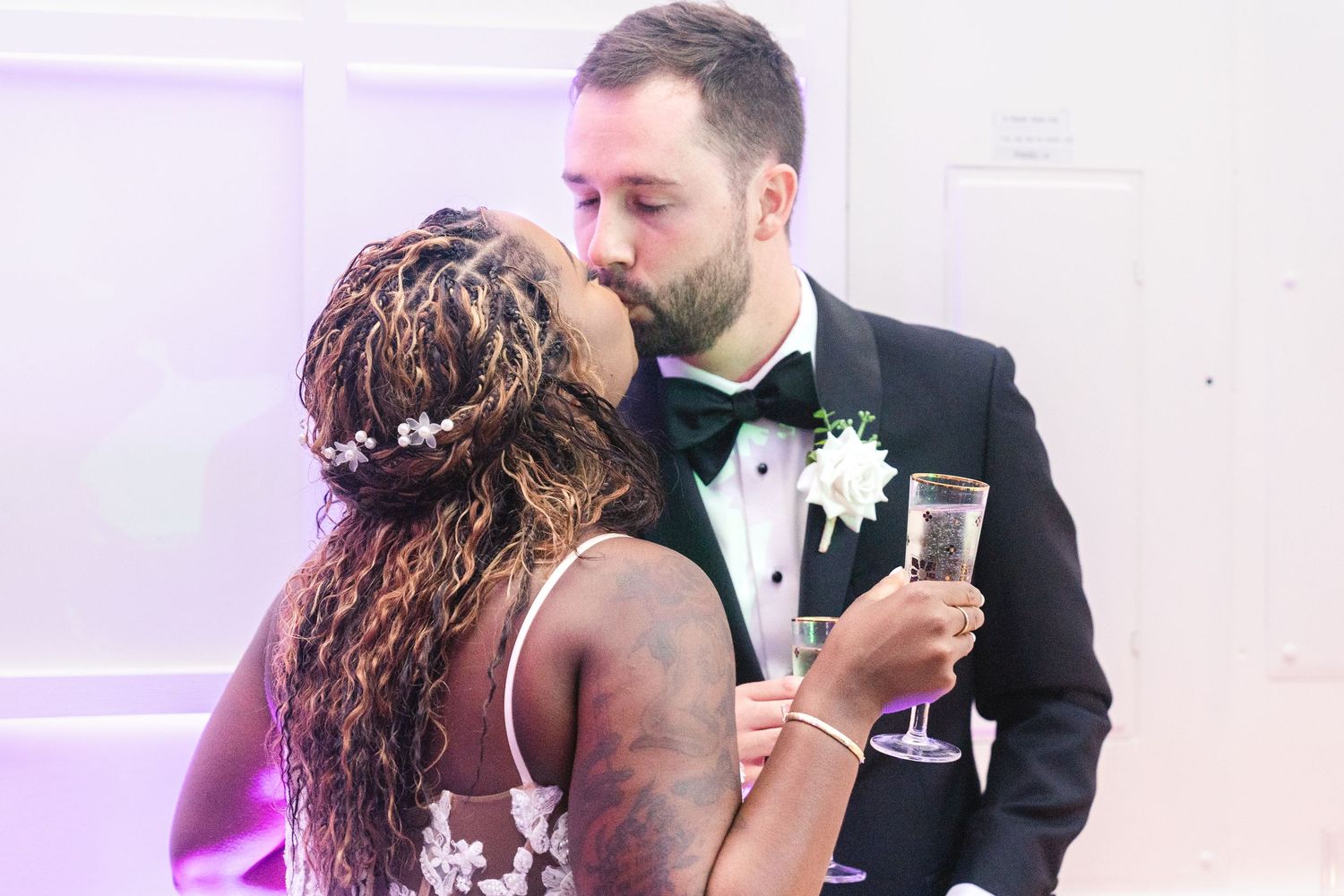 A couple shares a romantic dance together at their wedding reception with purple lighting in the background.