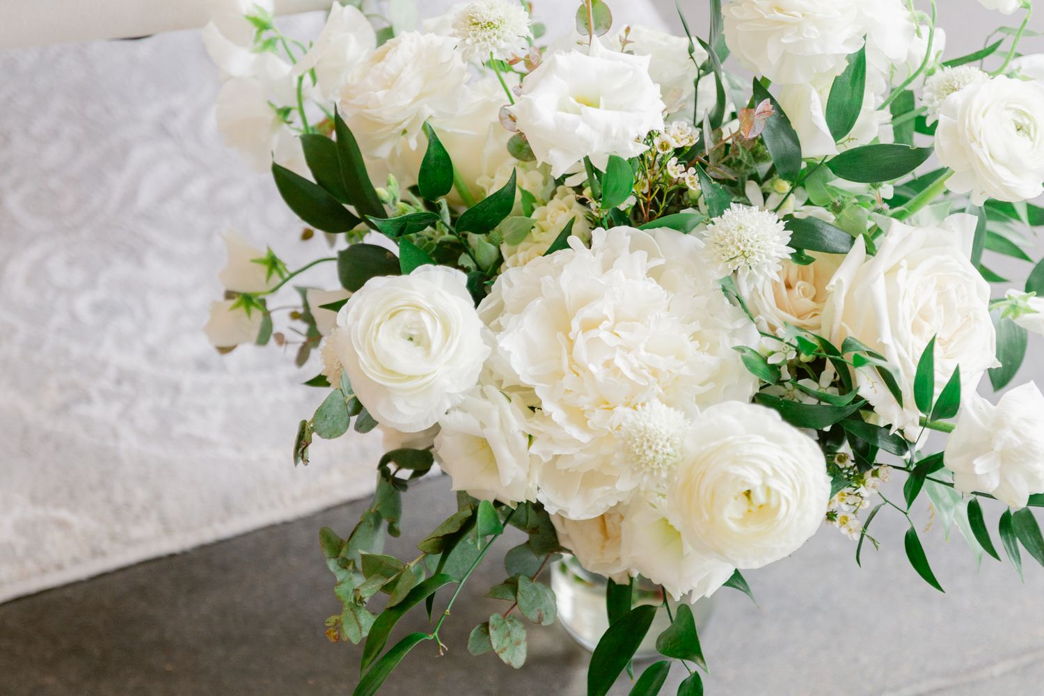 Elegant white roses and delicate greenery arranged in a romantic floral wedding centerpiece on a light background.