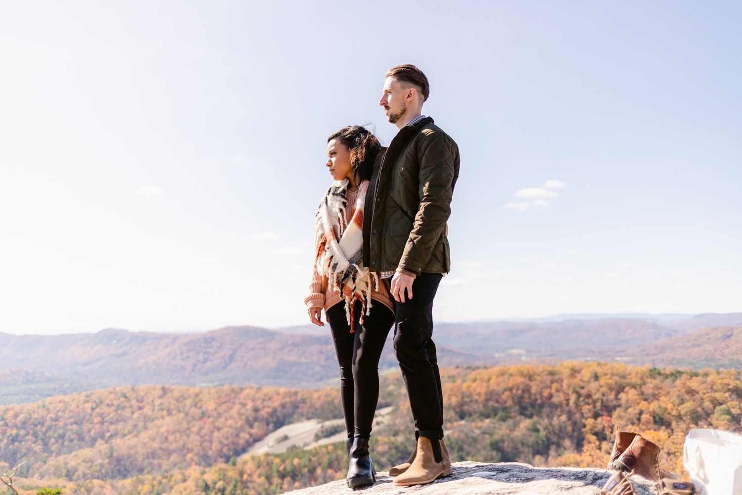 A couple embraces on a mountaintop overlook during autumn with scenic fall foliage views in the background.