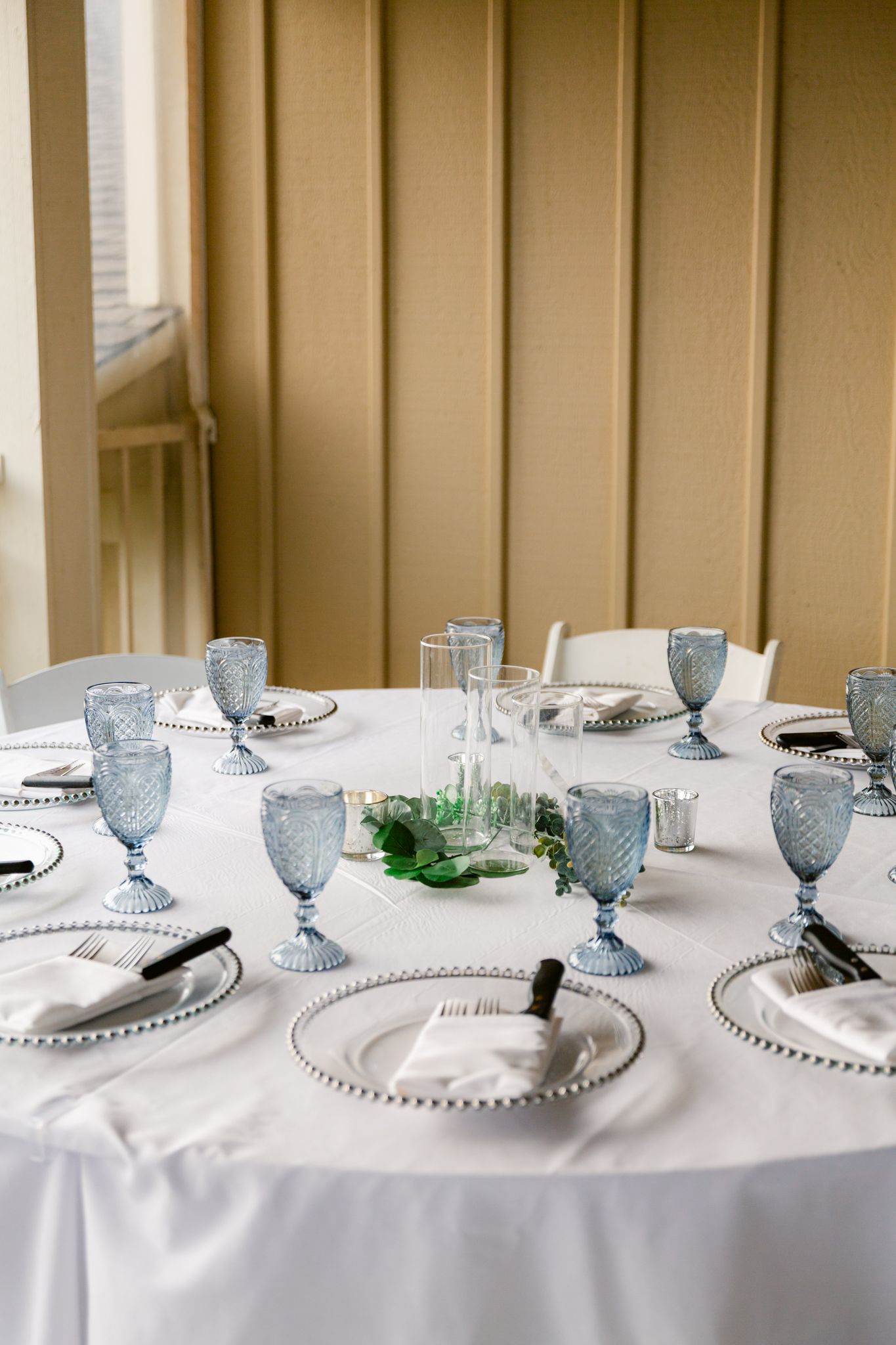 Elegant wedding reception table setting with blue glasses, white plates, and beaded charger plates.