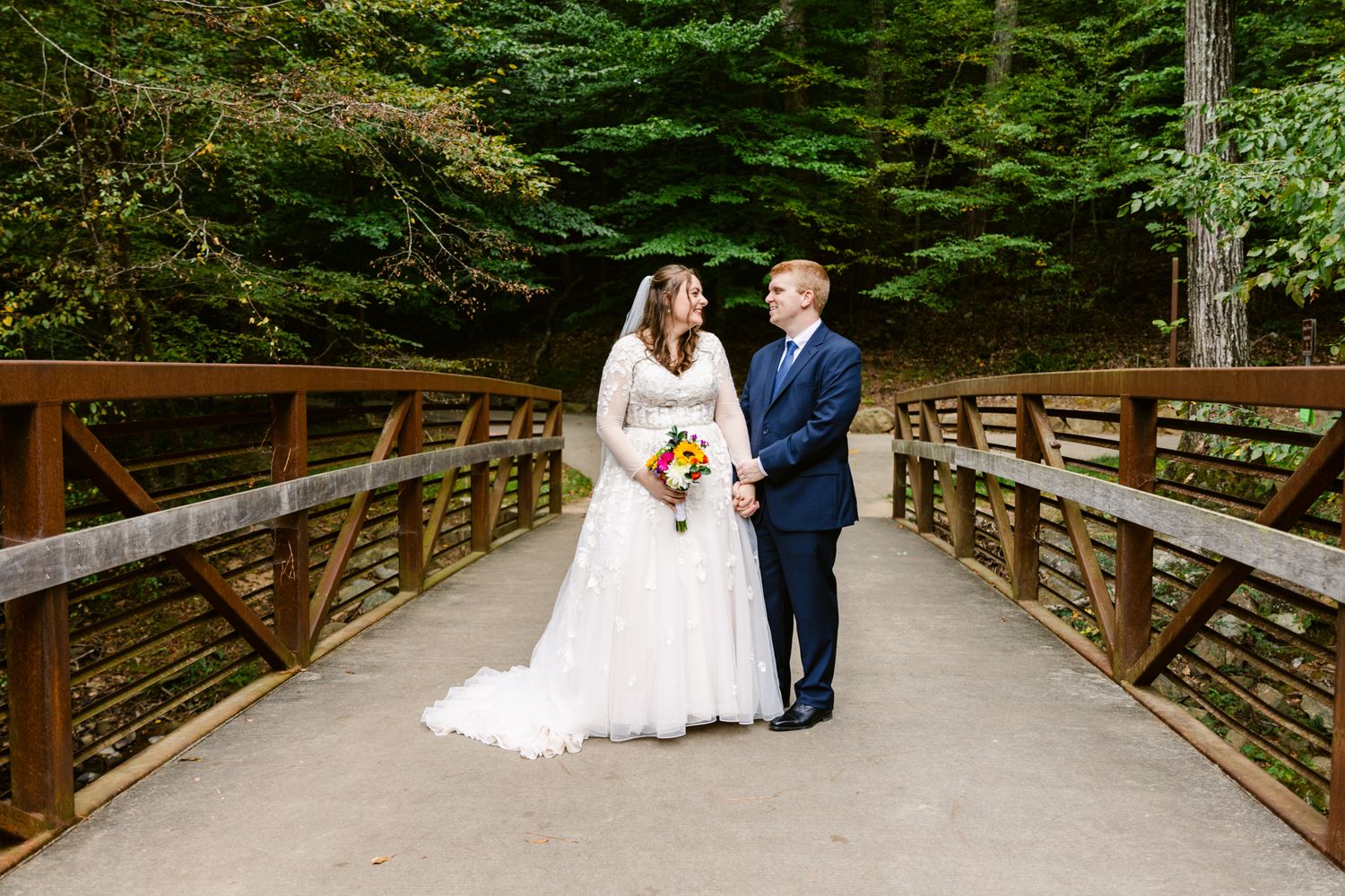 A couple shares a romantic moment on a wooden bridge surrounded by lush forest scenery.