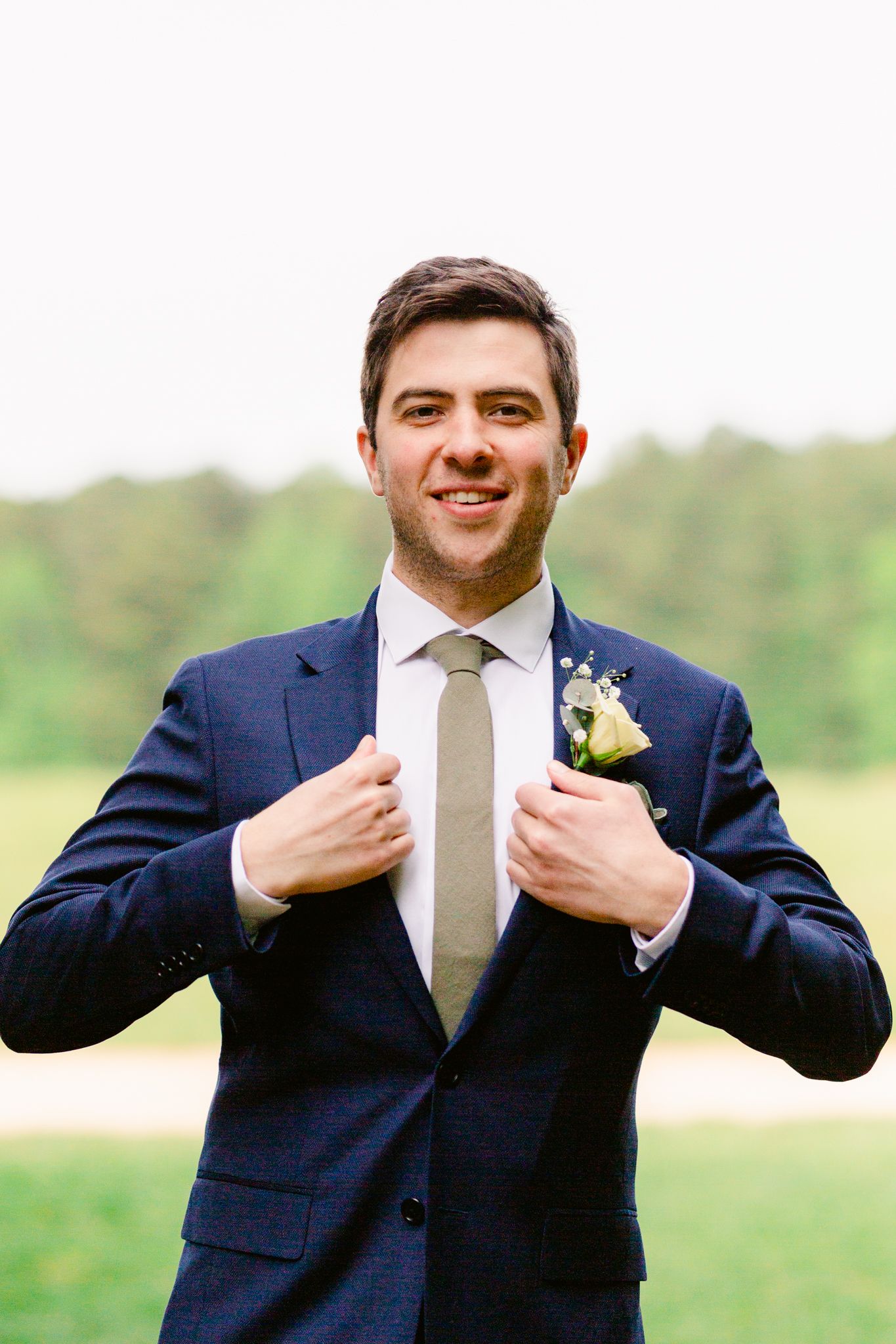 A groom in a navy suit adjusts his tie in a sequence of four candid photos outdoors.