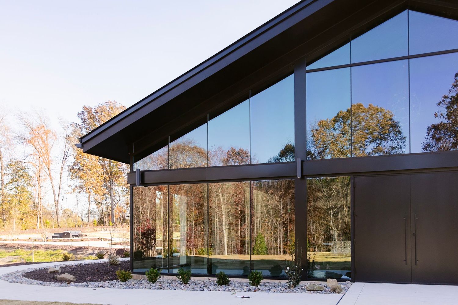 Modern black building with angled roof and large glass windows reflects sunlight against snowy winter landscape.
