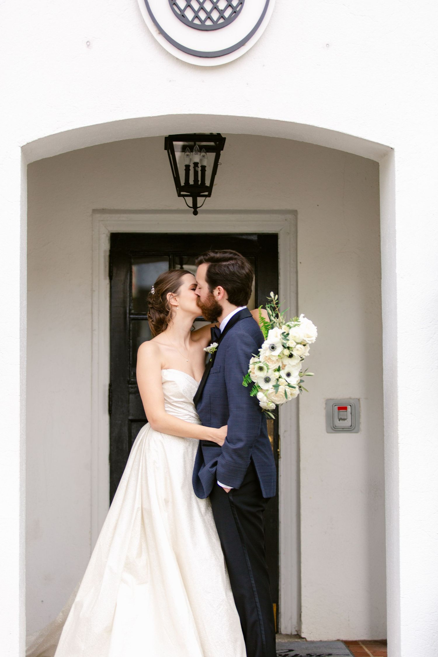 A couple shares a romantic kiss under a white archway during their wedding ceremony.