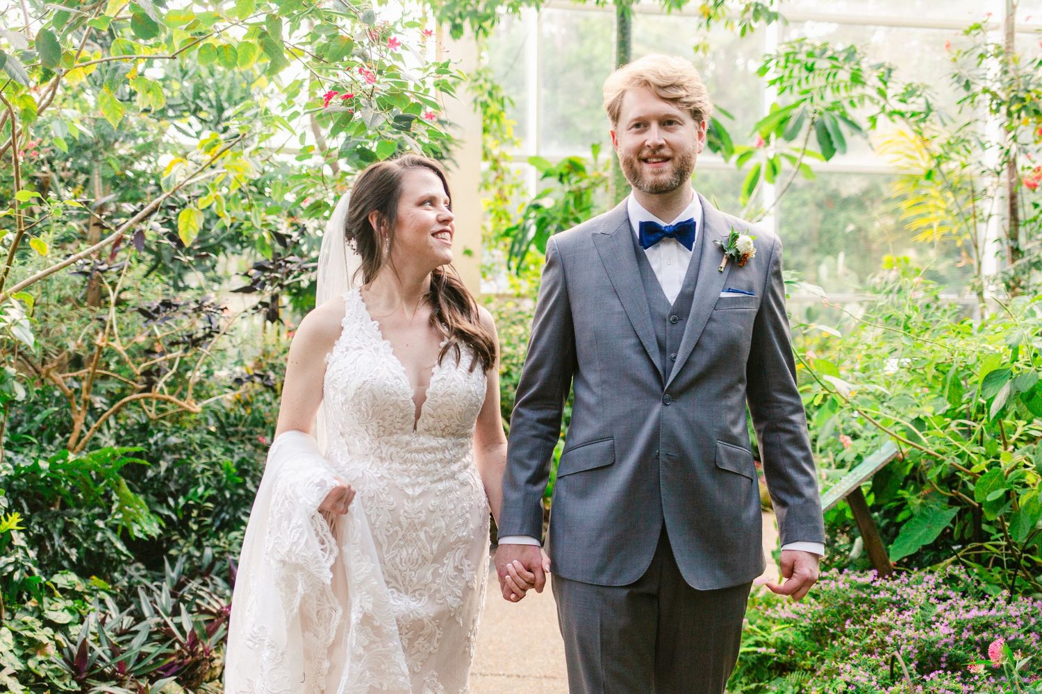Couple walking and laughing together in a lush garden setting with greenery and flowers in the background.