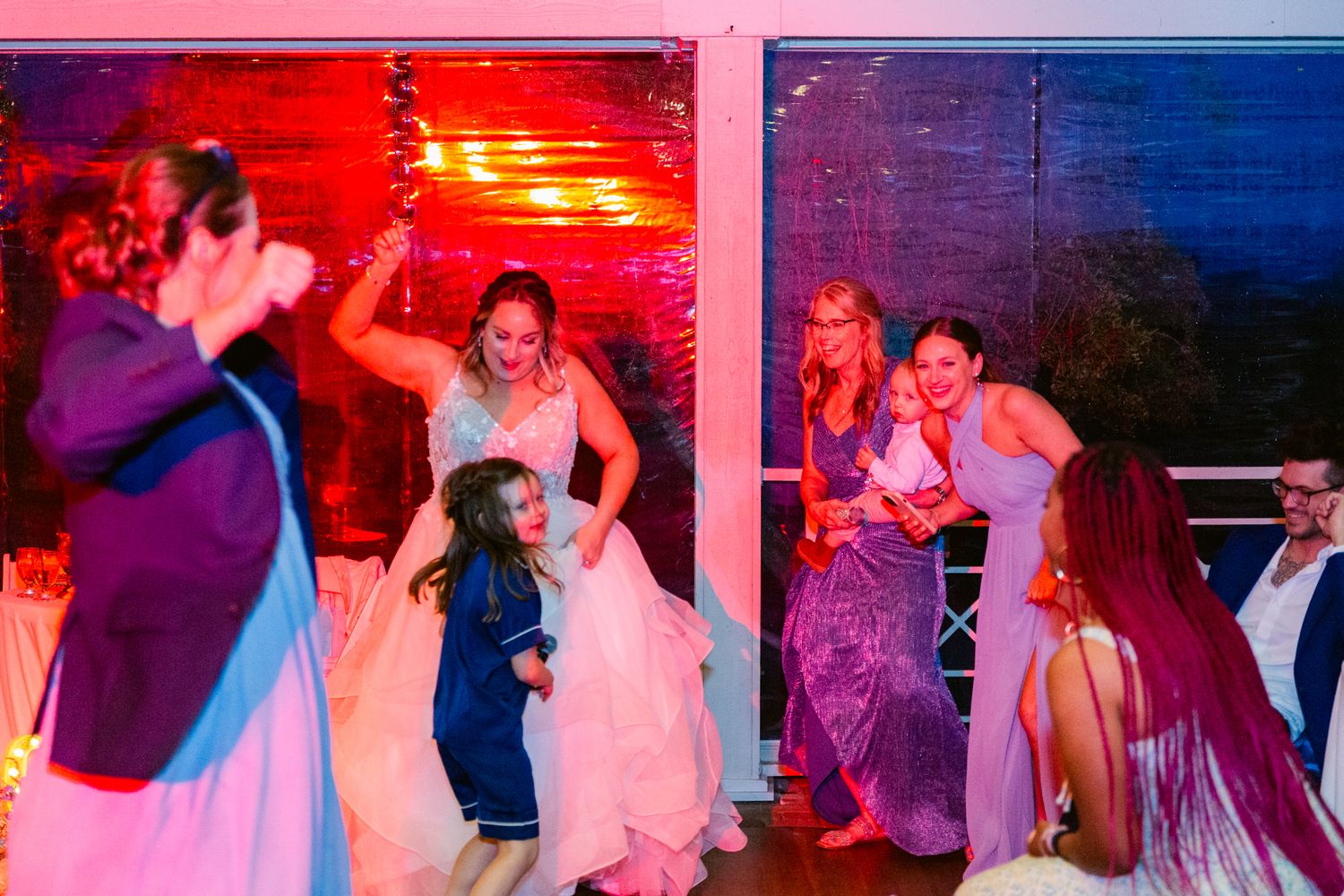 Couples dancing together at a wedding reception with colorful red and blue lighting effects creating a romantic atmosphere.