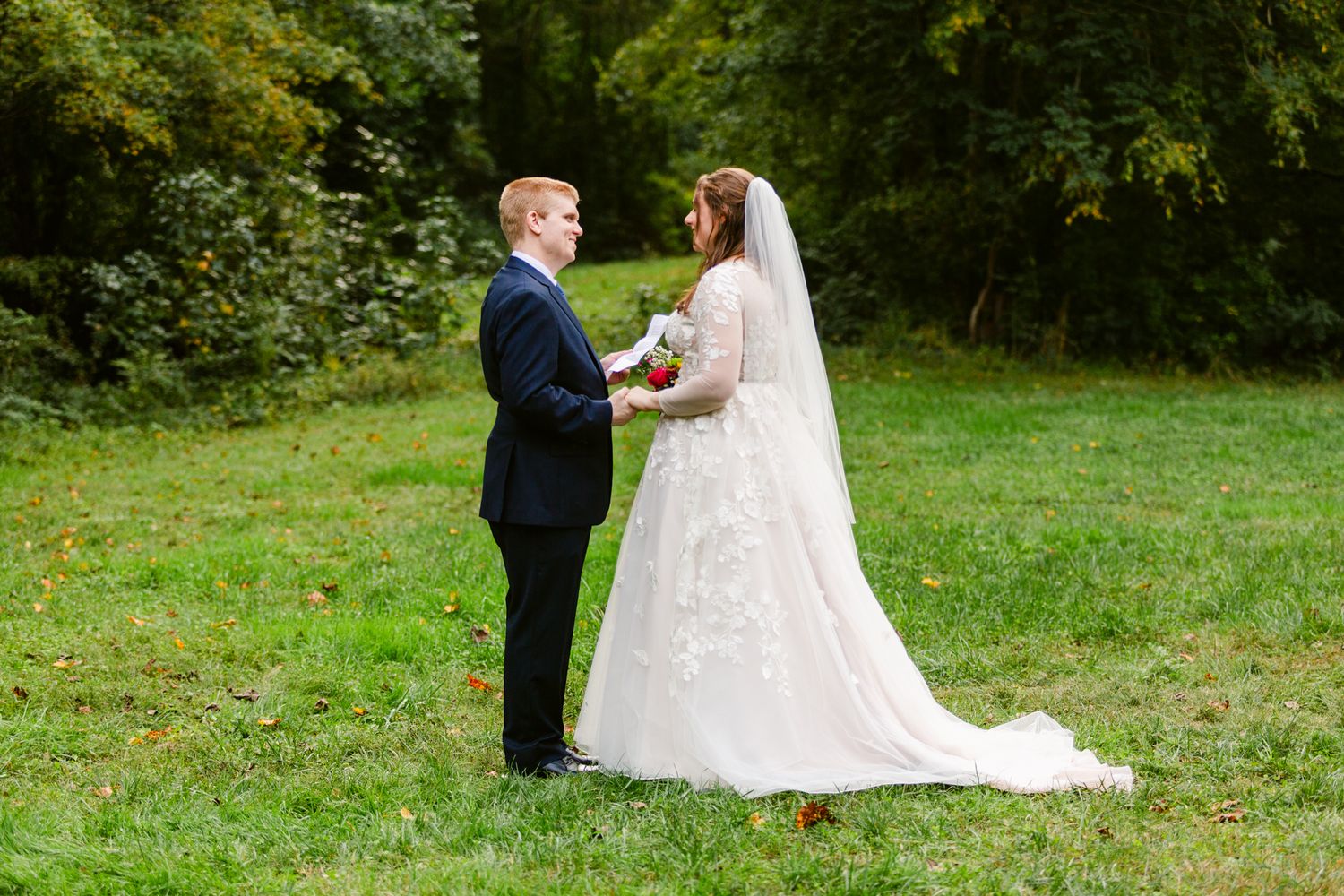 A couple in wedding attire shares a romantic moment together in a lush green outdoor garden setting.