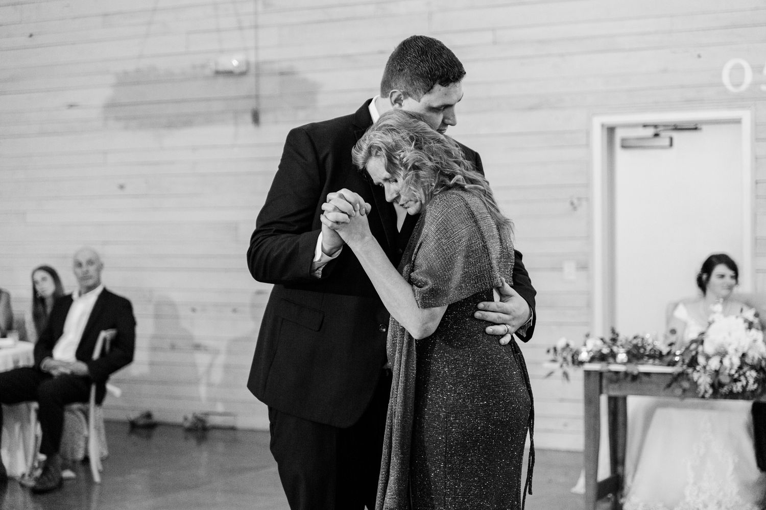 A romantic slow dance between a couple at a wedding reception in a rustic barn venue.