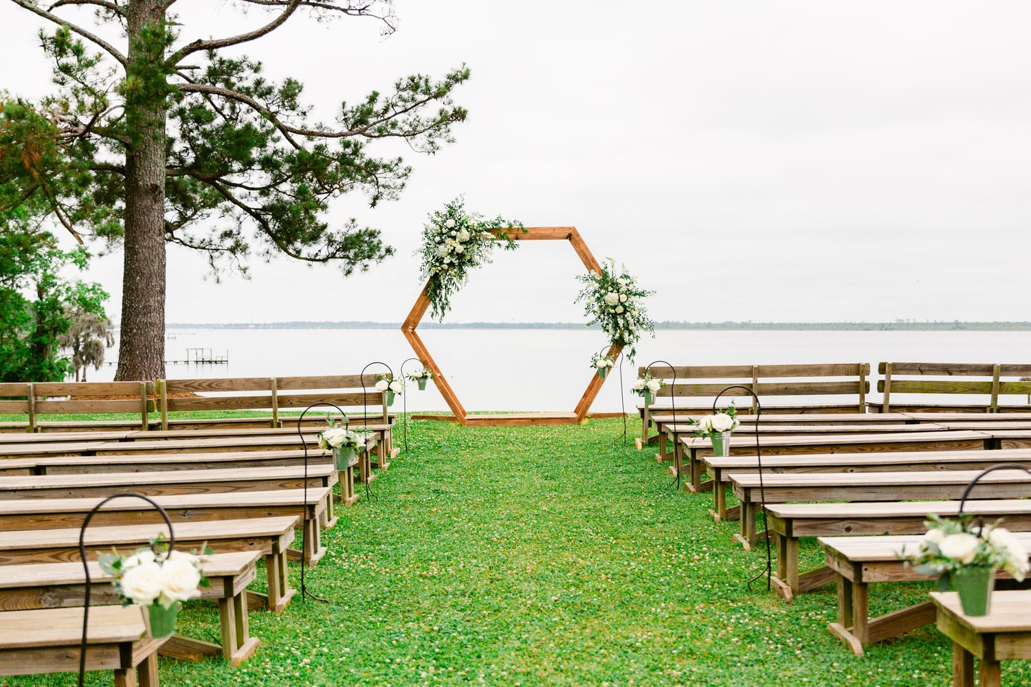 Rustic wooden benches arranged in rows for an outdoor ceremony with a lake view and trees in the background.