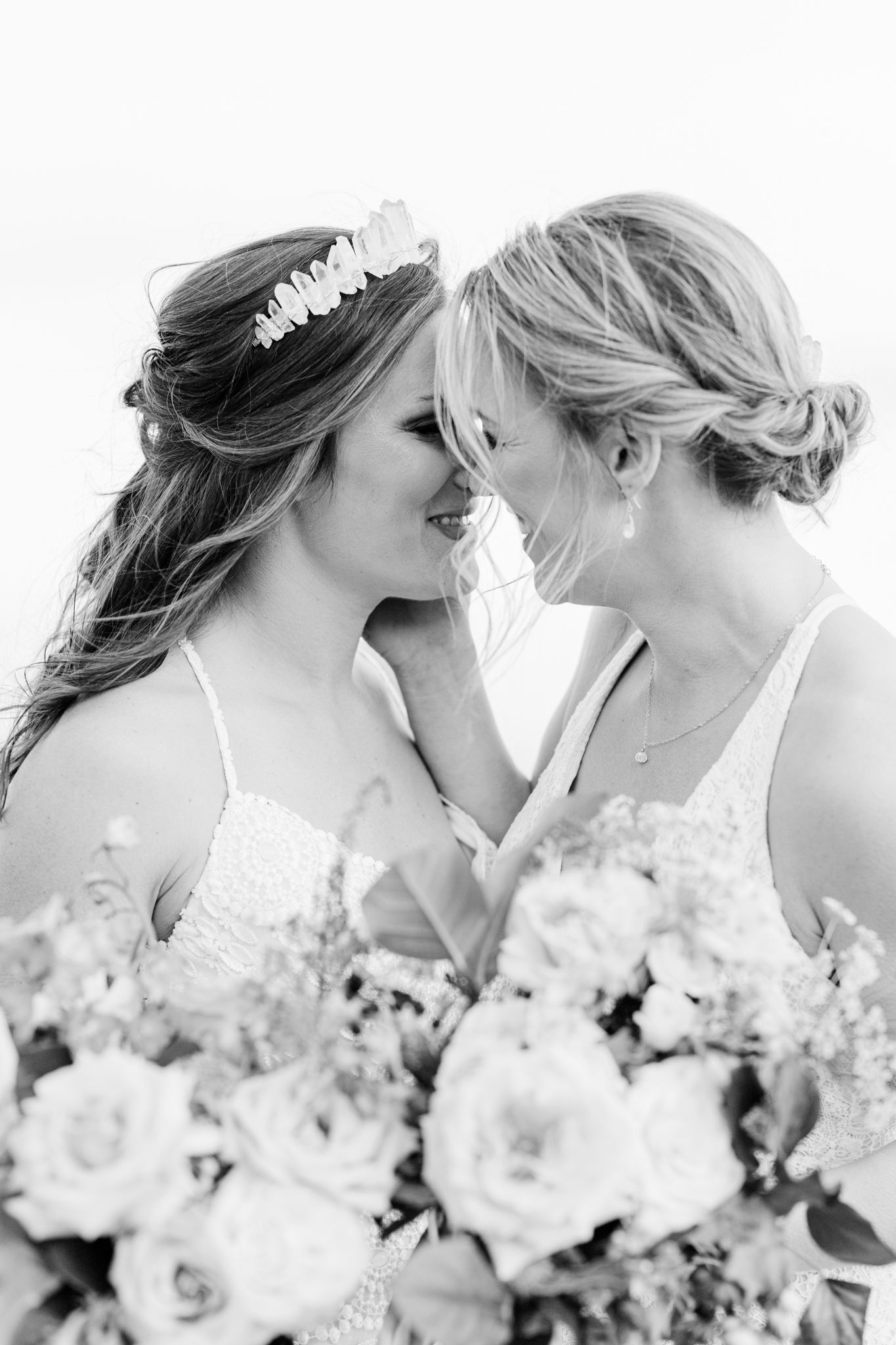 Row of bridesmaids in white dresses holding bouquets while posing together outdoors.