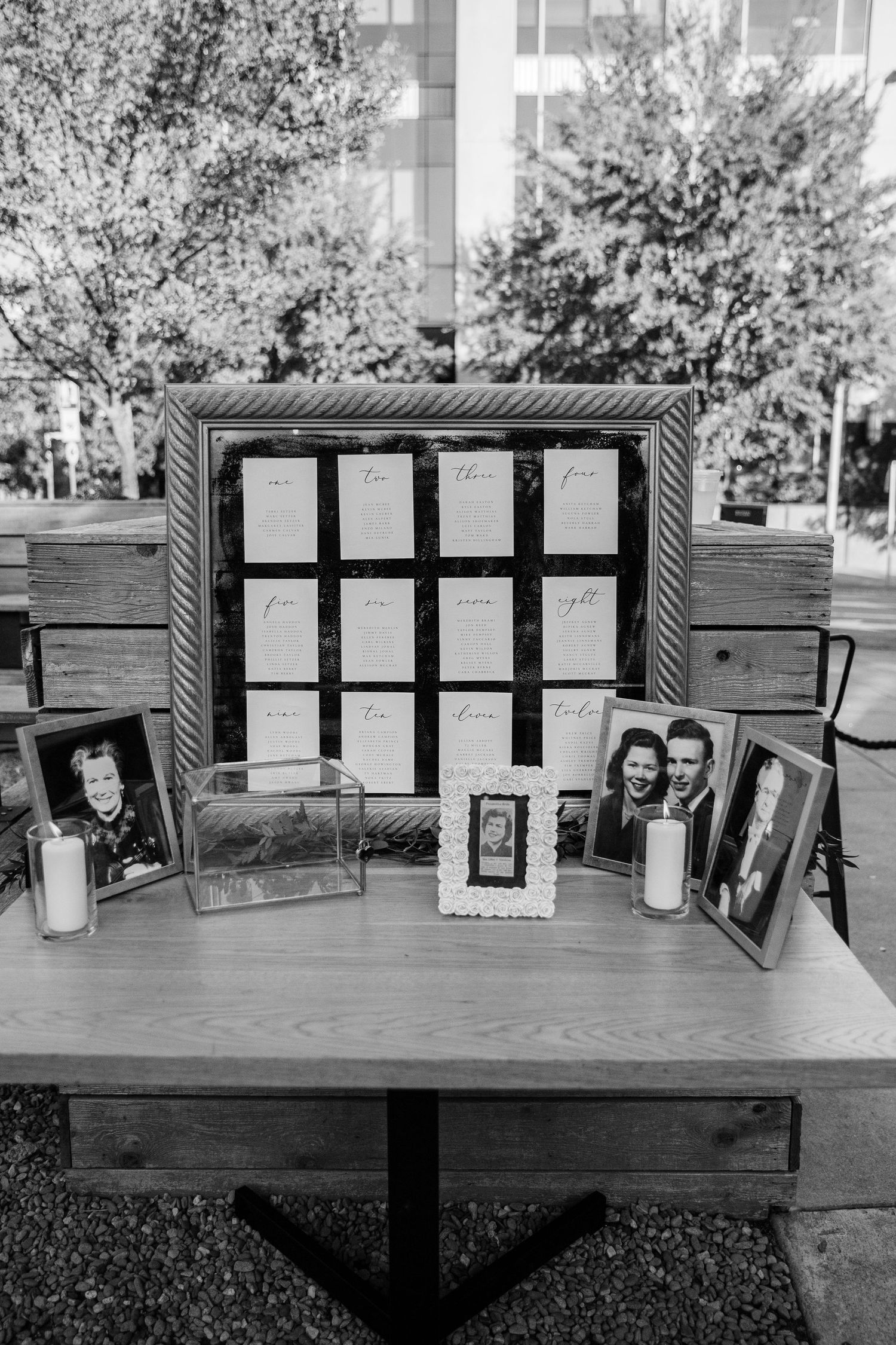 Wedding seating chart display with framed photos and decorative elements on a wooden table outdoors.
