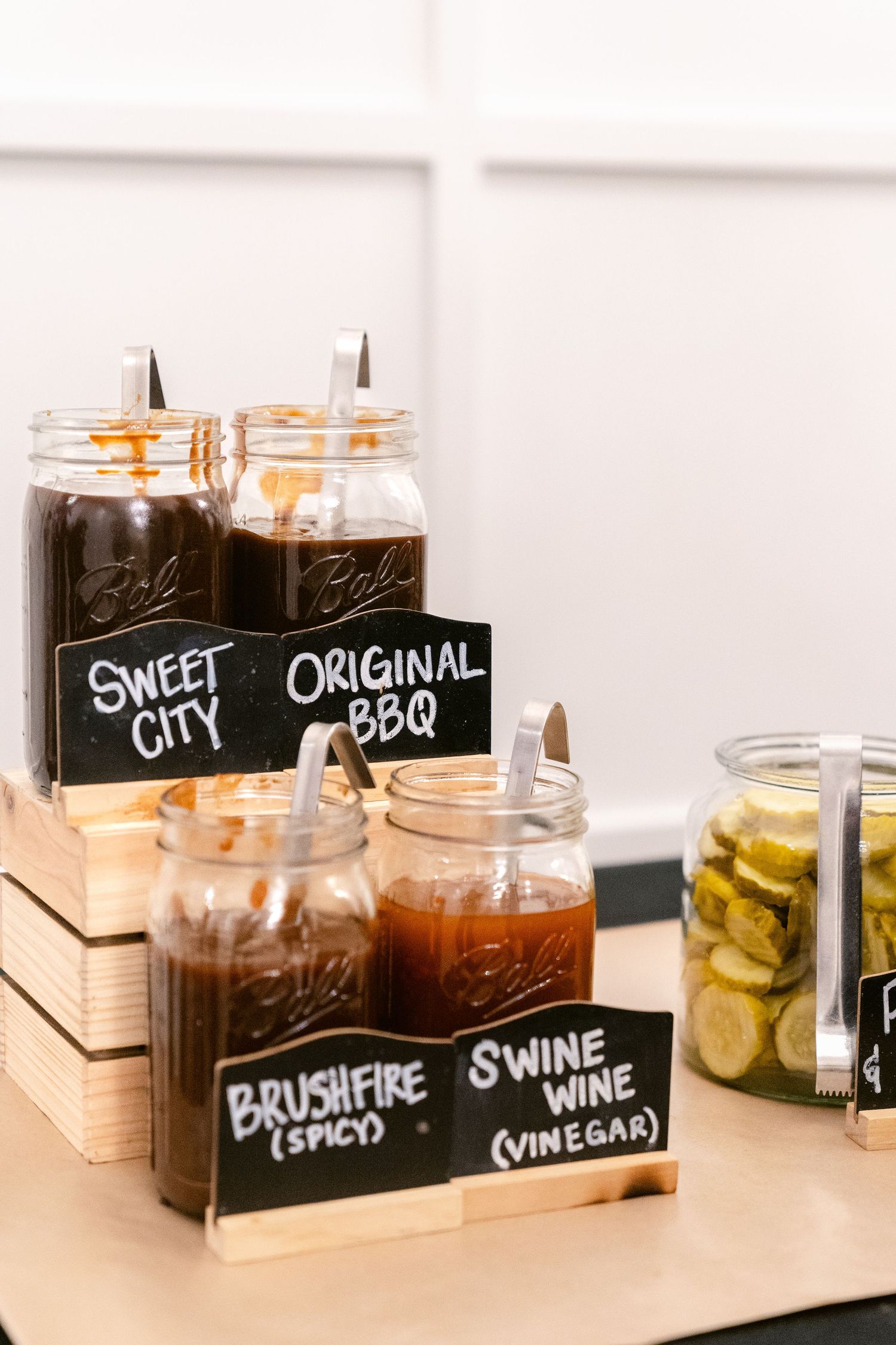Glass jars with chalkboard labels containing different vinegars and condiments displayed in wooden holders.