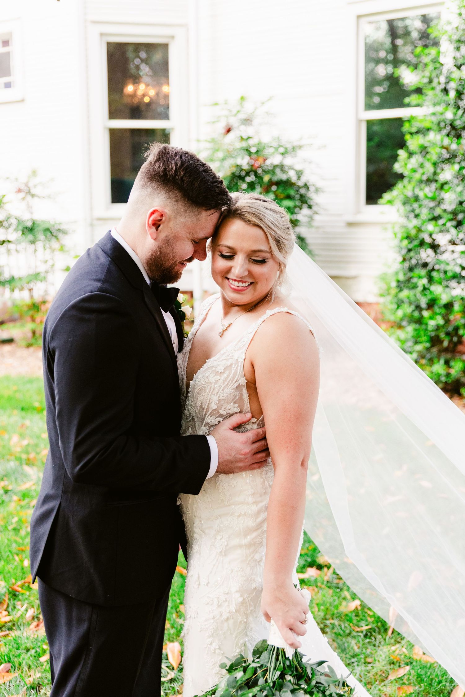 A romantic outdoor wedding photoshoot with a flowing veil and lush greenery in the background.