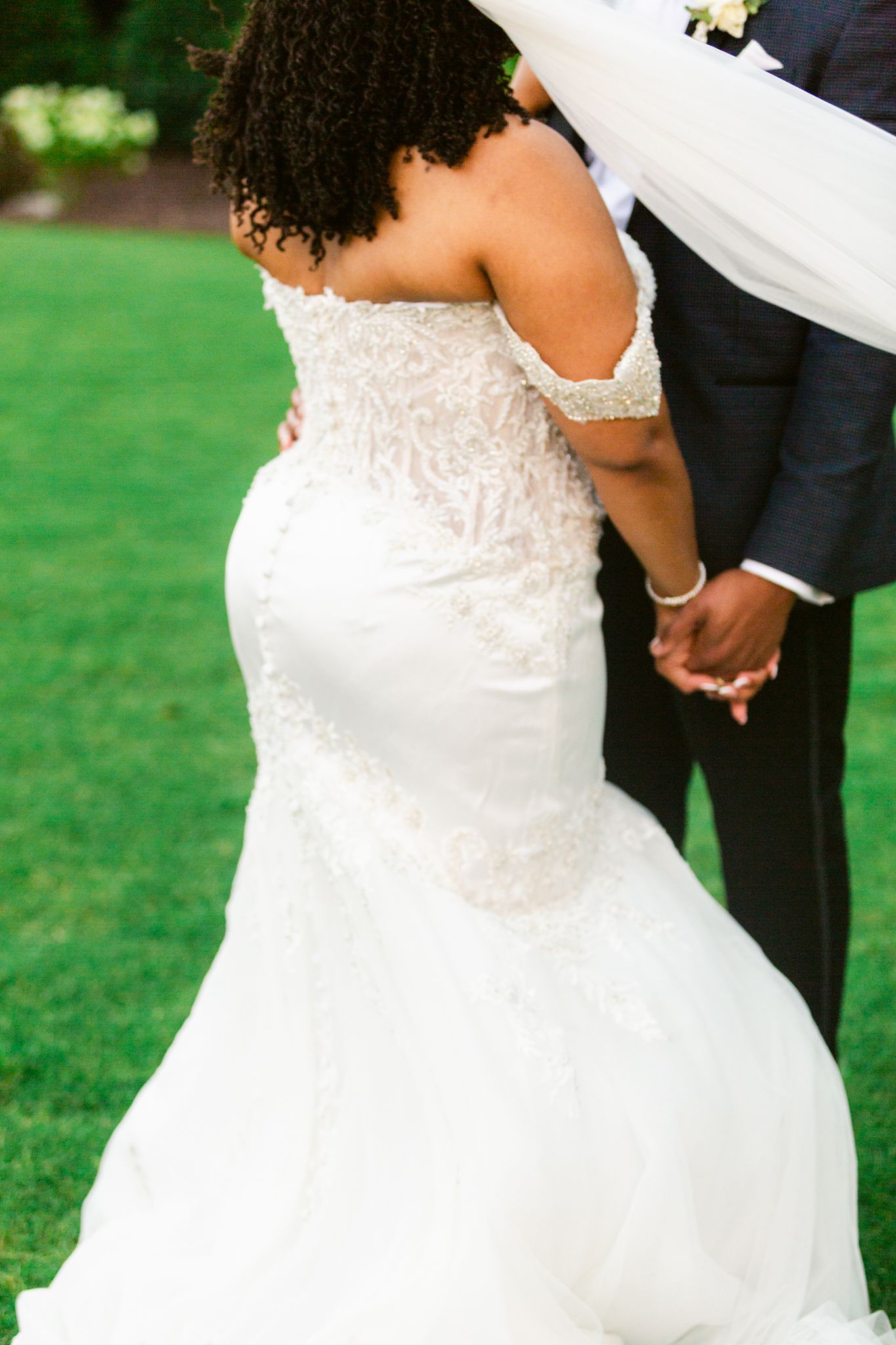 Close-up details of a bride's elegant lace wedding dress with delicate beading and embellishments in an outdoor setting.