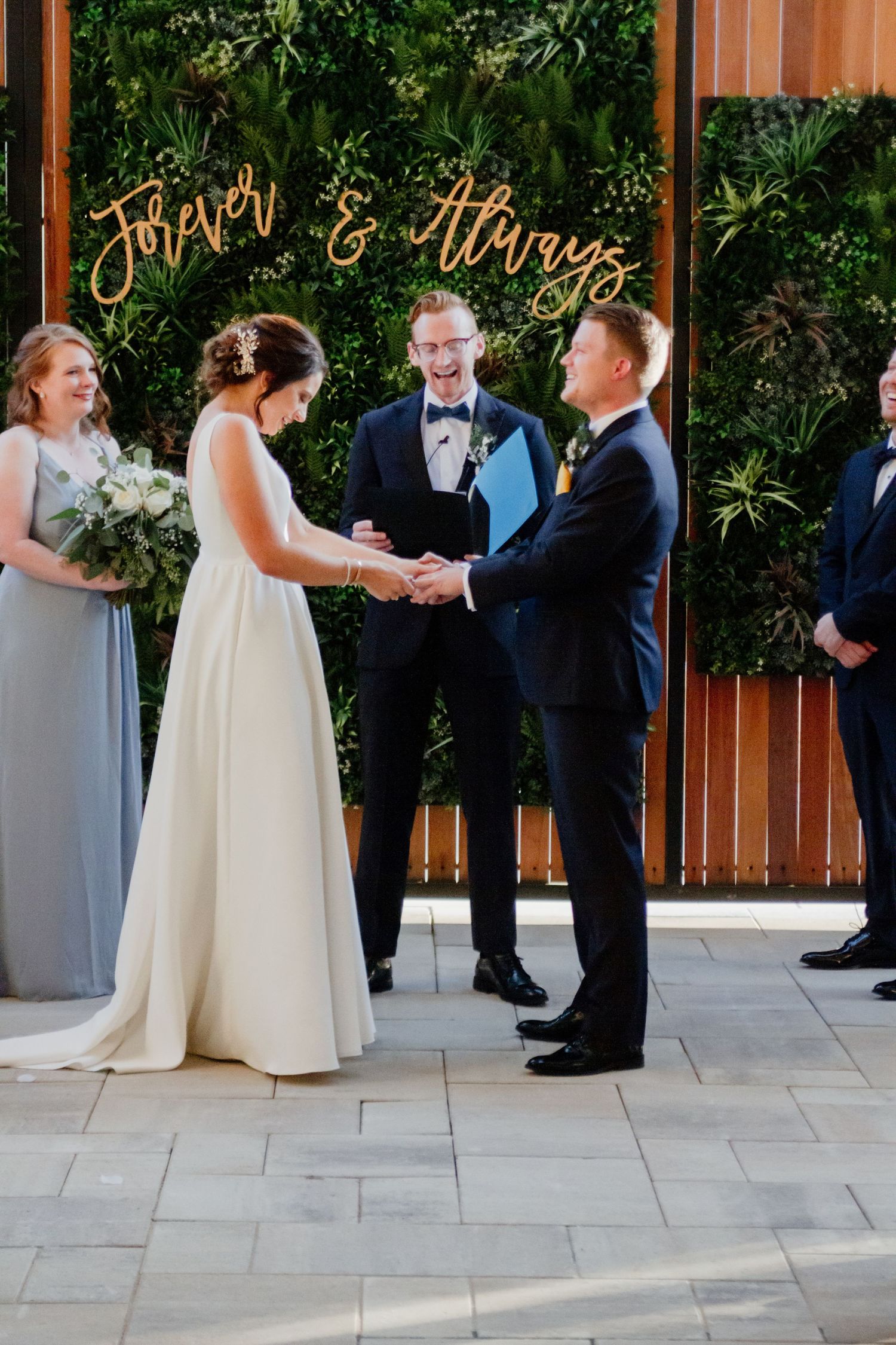 Wedding ceremony under gold 'Forever & Always' sign with greenery wall backdrop.