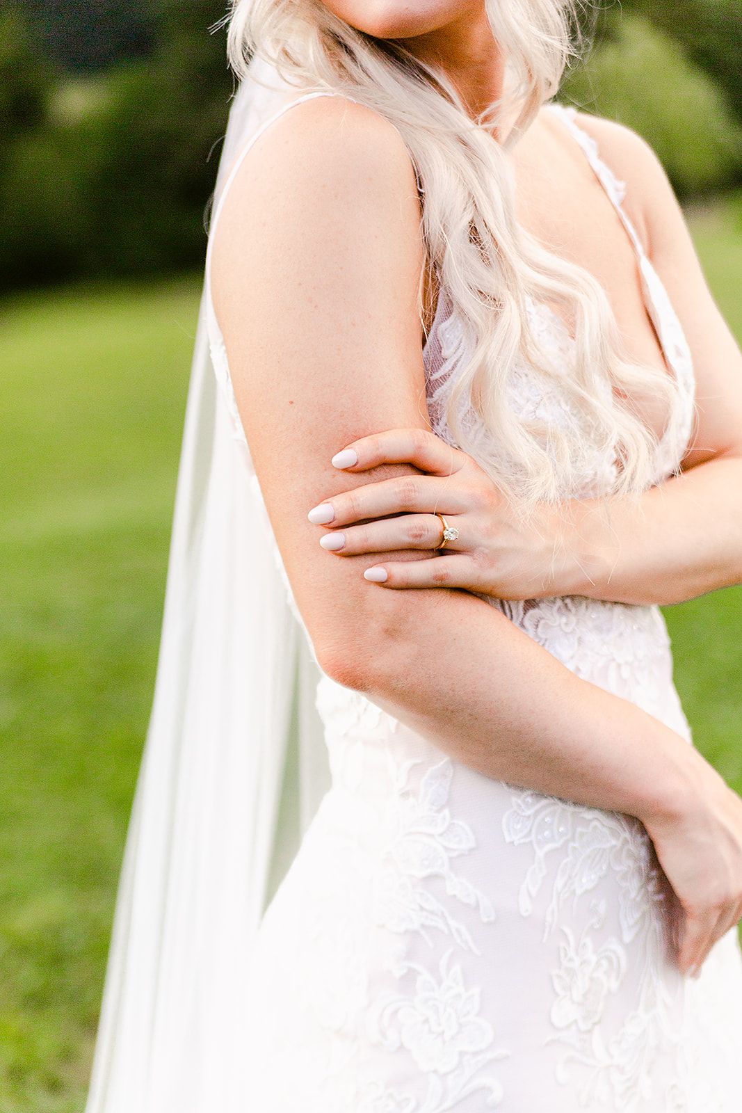 Delicate lace detailing on fitted wedding dress with sheer veil in outdoor setting.