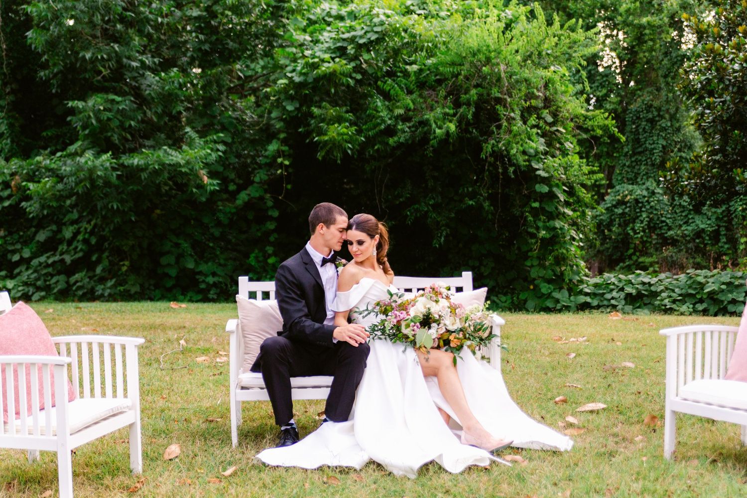 Garden wedding setup with white benches arranged on green lawn.