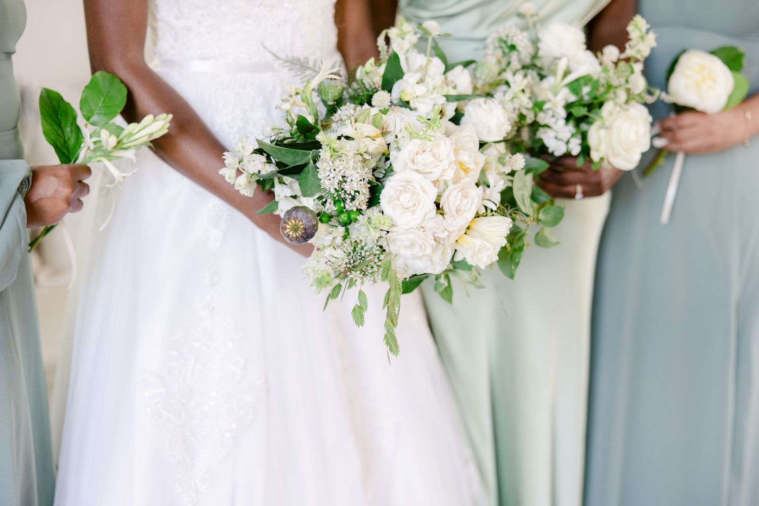 Line of bridesmaids holding white and green floral bouquets against light blue background.