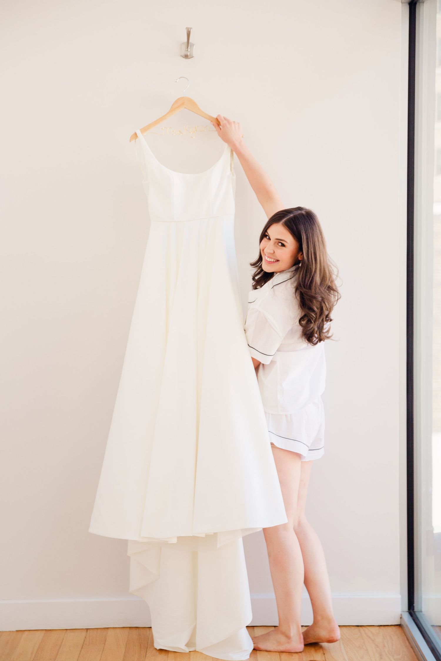 A person in casual attire admires a white wedding dress hanging on display.
