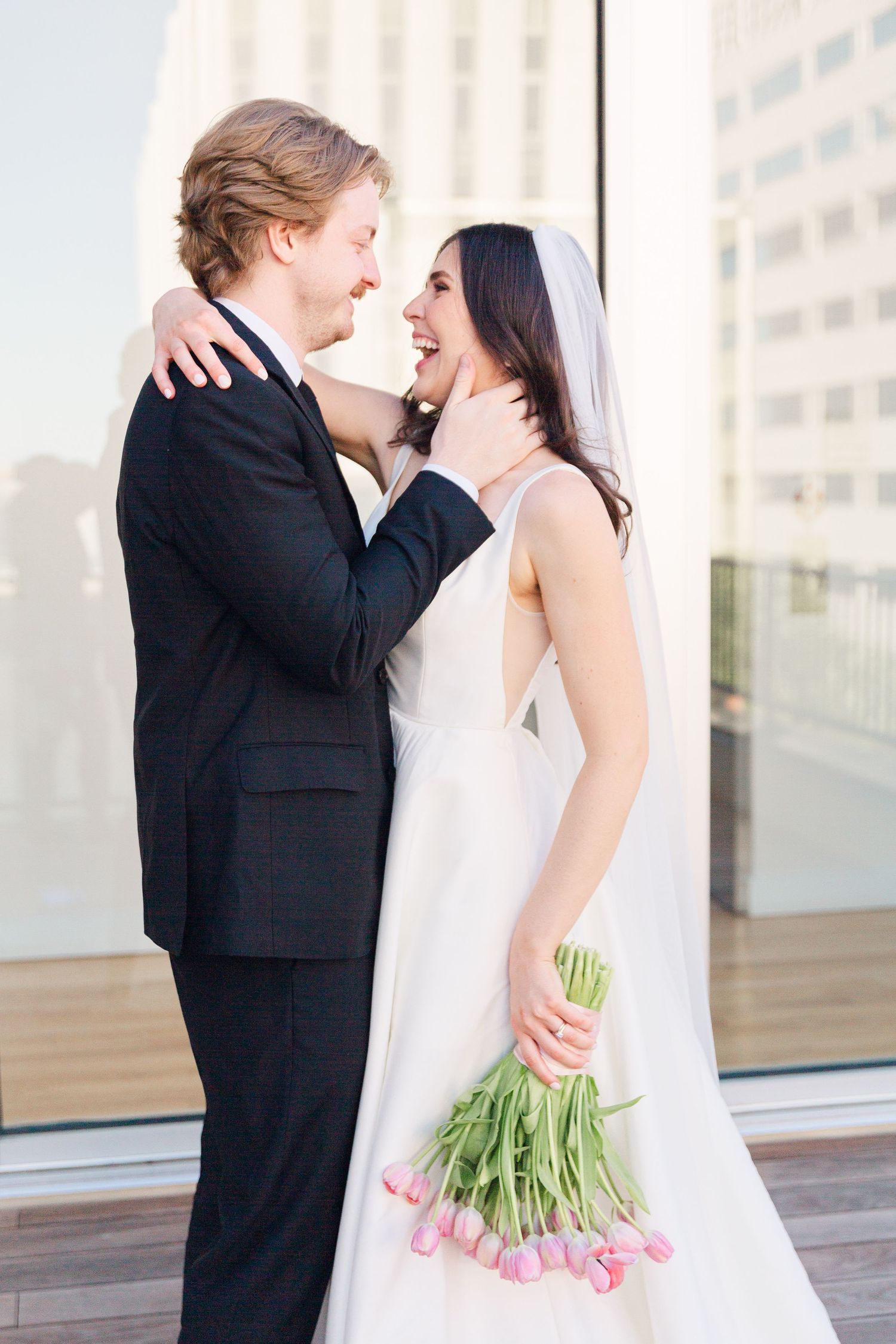 A romantic wedding portrait with the couple embracing and laughing while holding pink tulips.