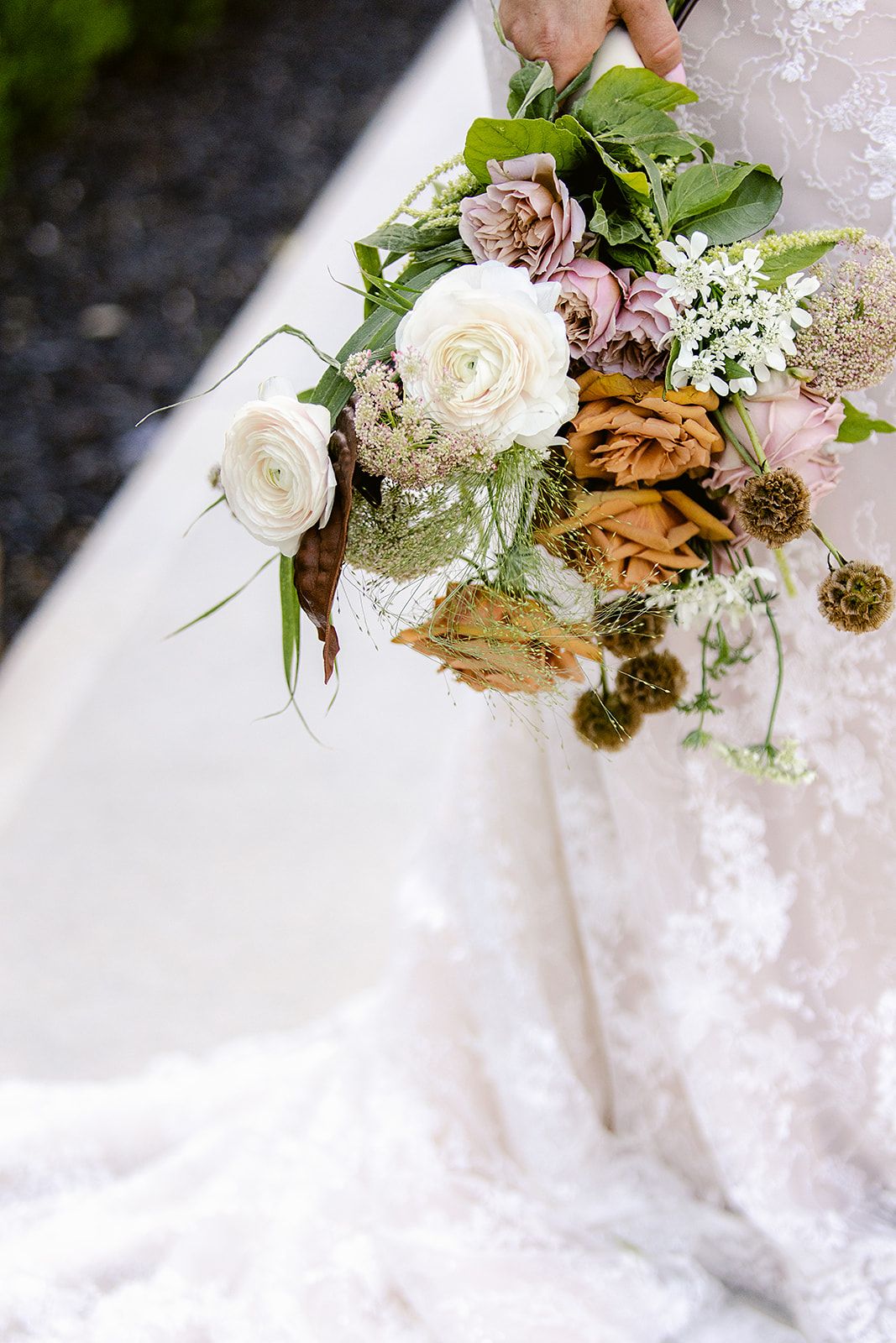 Delicate floral arrangement with white and pink roses, greenery, and natural elements on white lace fabric.