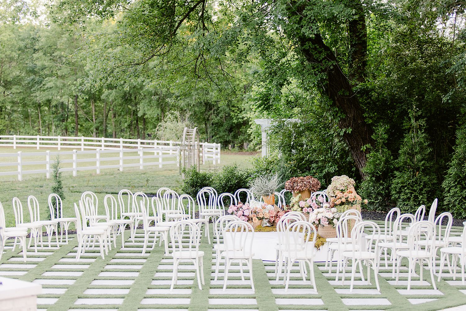 White chairs arranged in rows for an outdoor wedding ceremony under green trees and natural lighting.