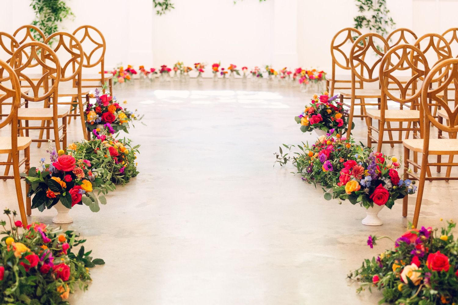 Elegant wedding ceremony setup with wooden chairs and vibrant floral arrangements along the aisle.