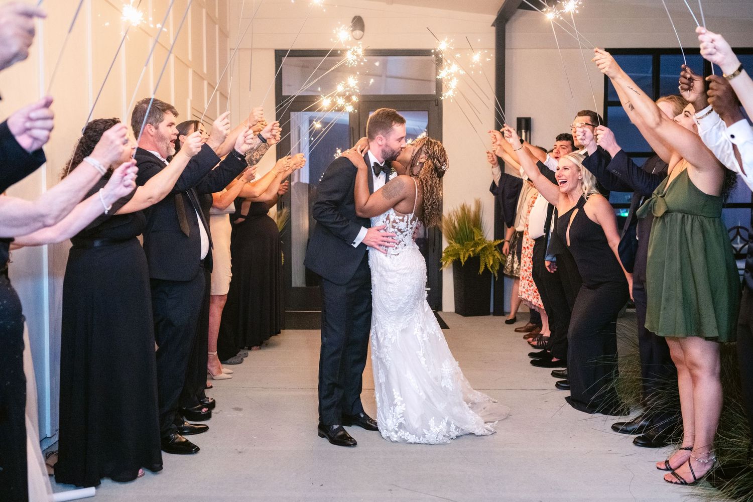 Wedding guests form a tunnel with raised arms as newlyweds dance beneath during reception celebration.
