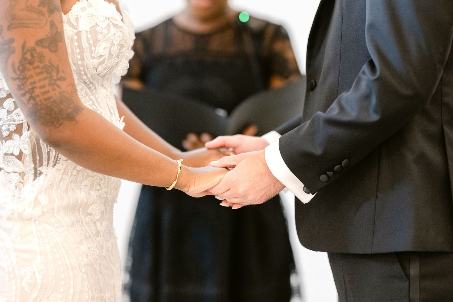 A couple holds hands during their wedding ceremony, with the bride wearing a white dress and veil.
