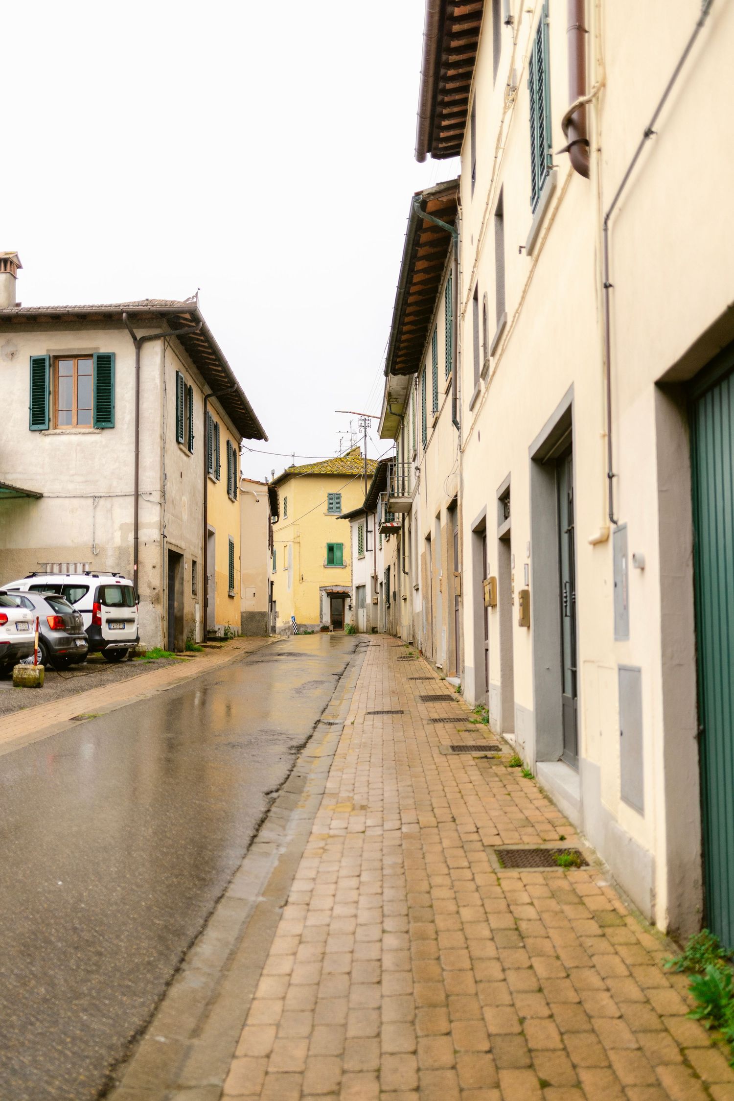 Narrow cobblestone street lined with traditional Italian buildings and white walls.