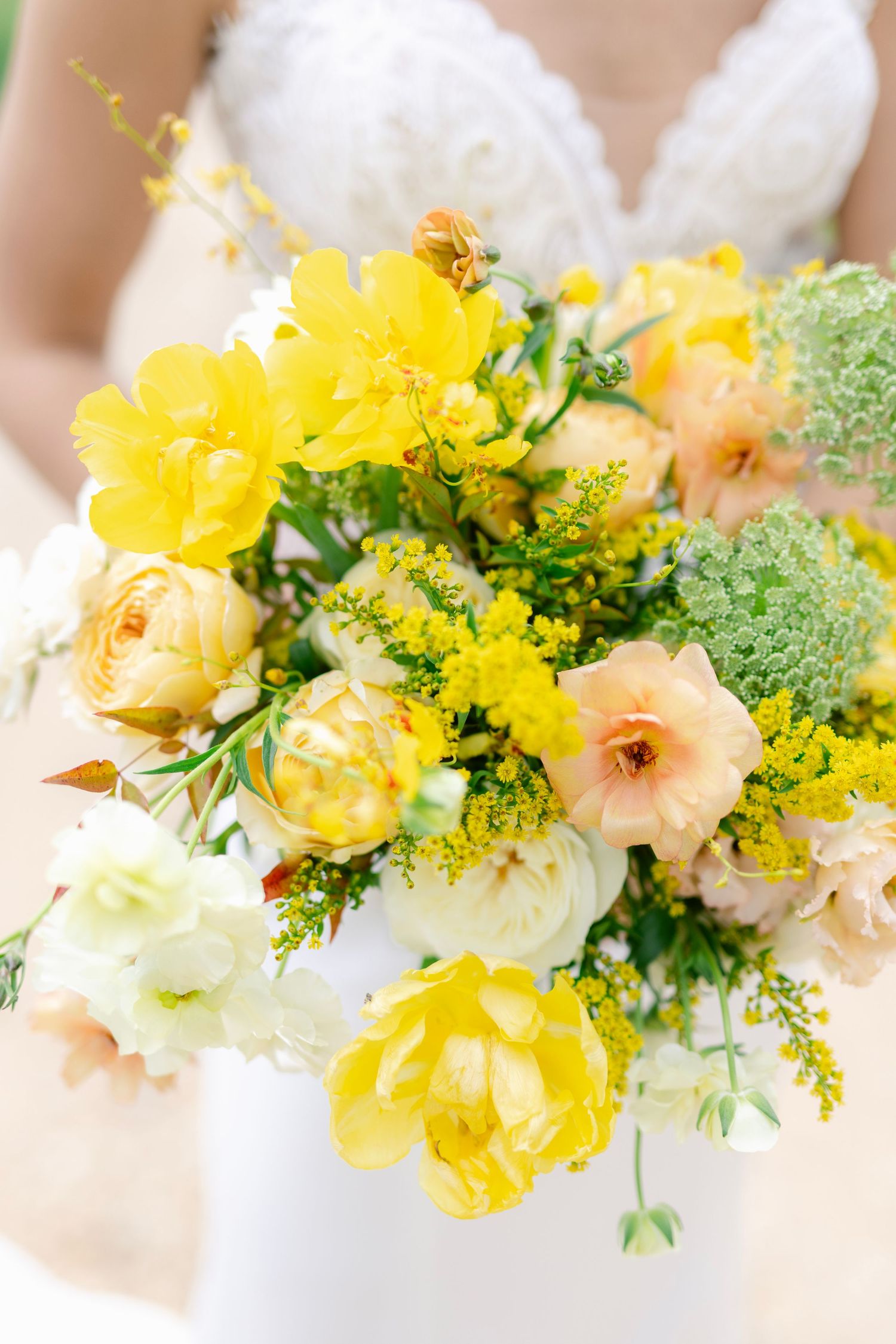 A vibrant spring wedding bouquet featuring yellow and peach flowers with delicate greenery accents.