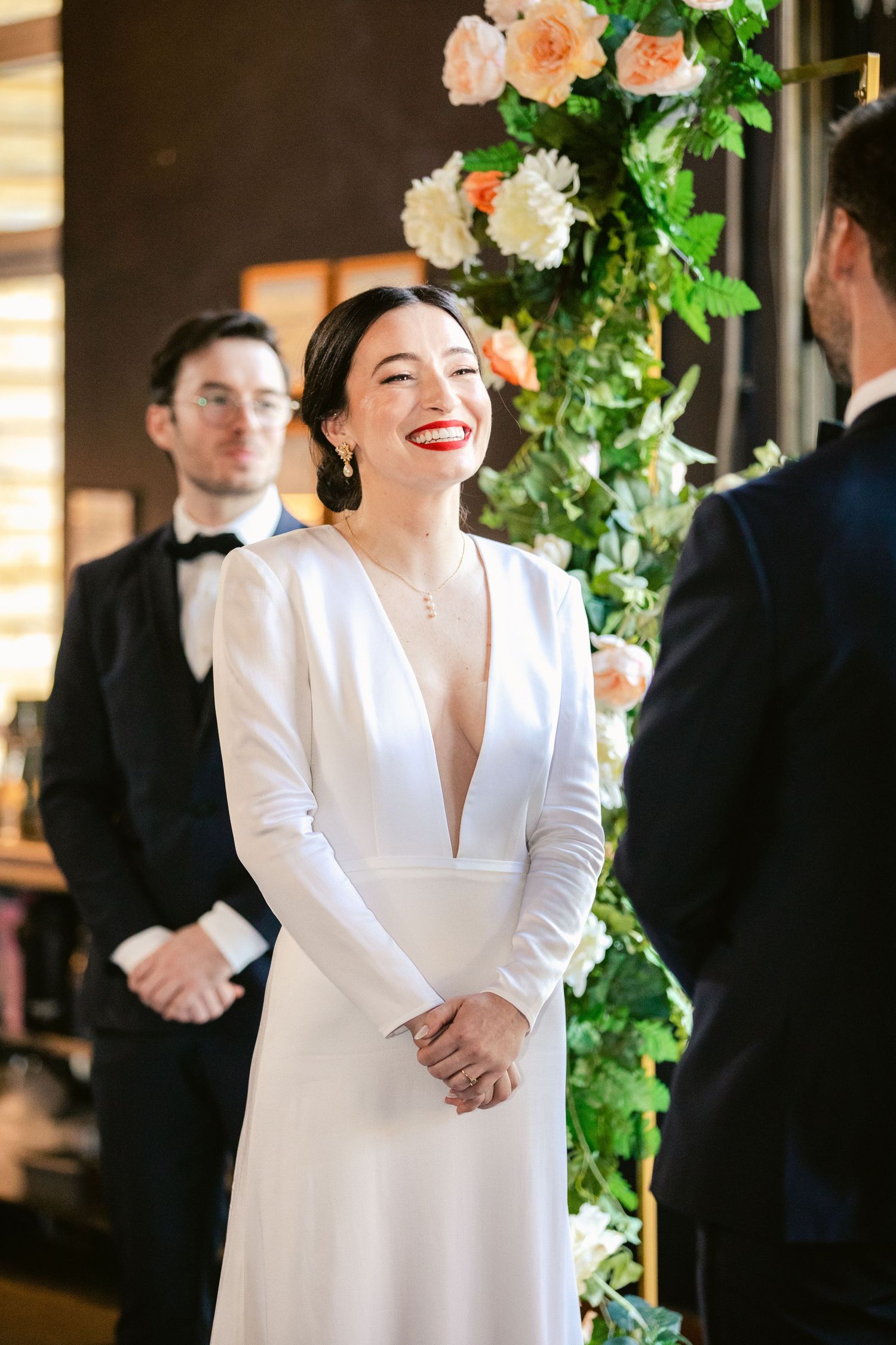 Elegant wedding scene with white gown and floral decor featuring peach roses and greenery in warm indoor lighting.