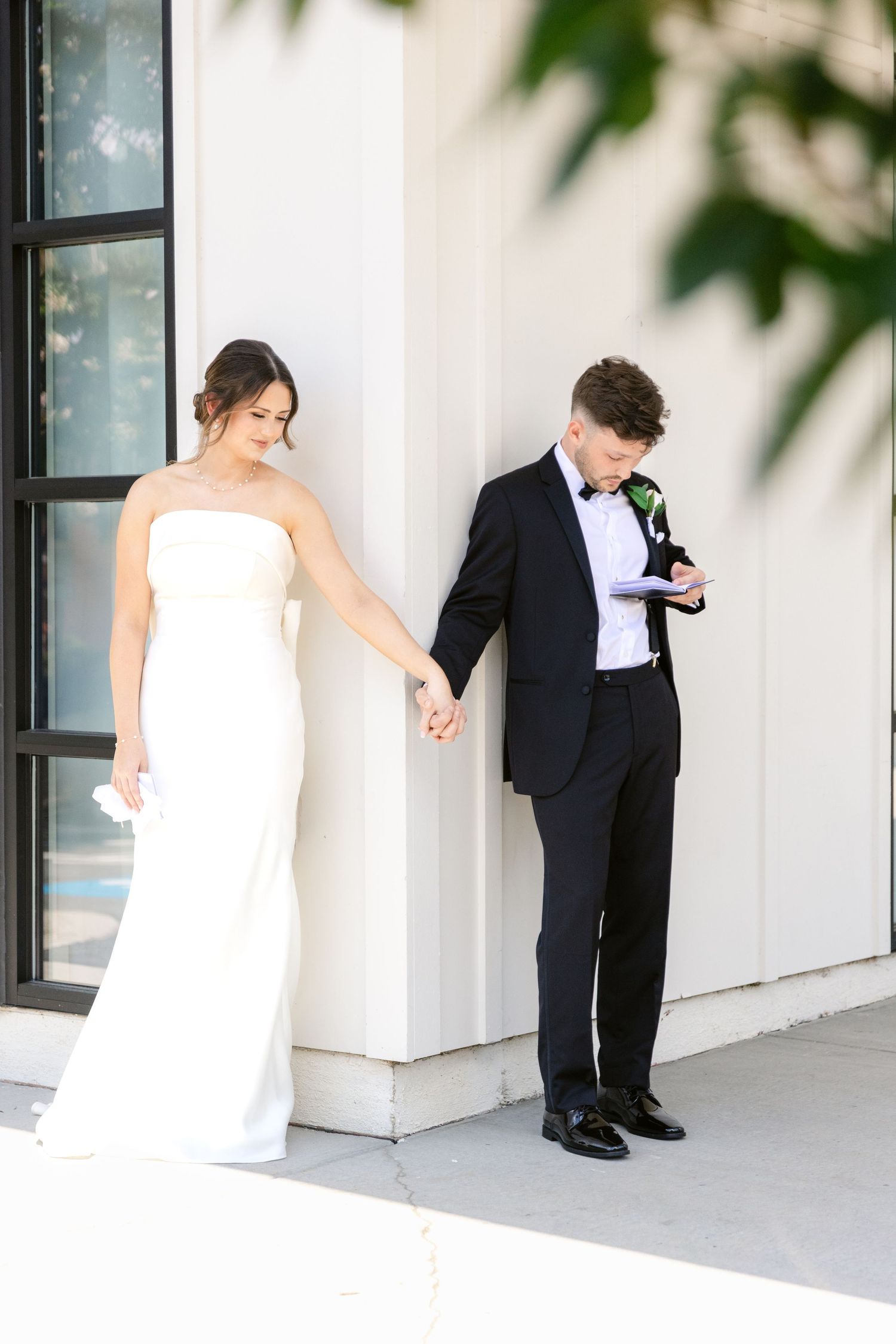 Playful wedding portraits against a modern white wall with architectural details.