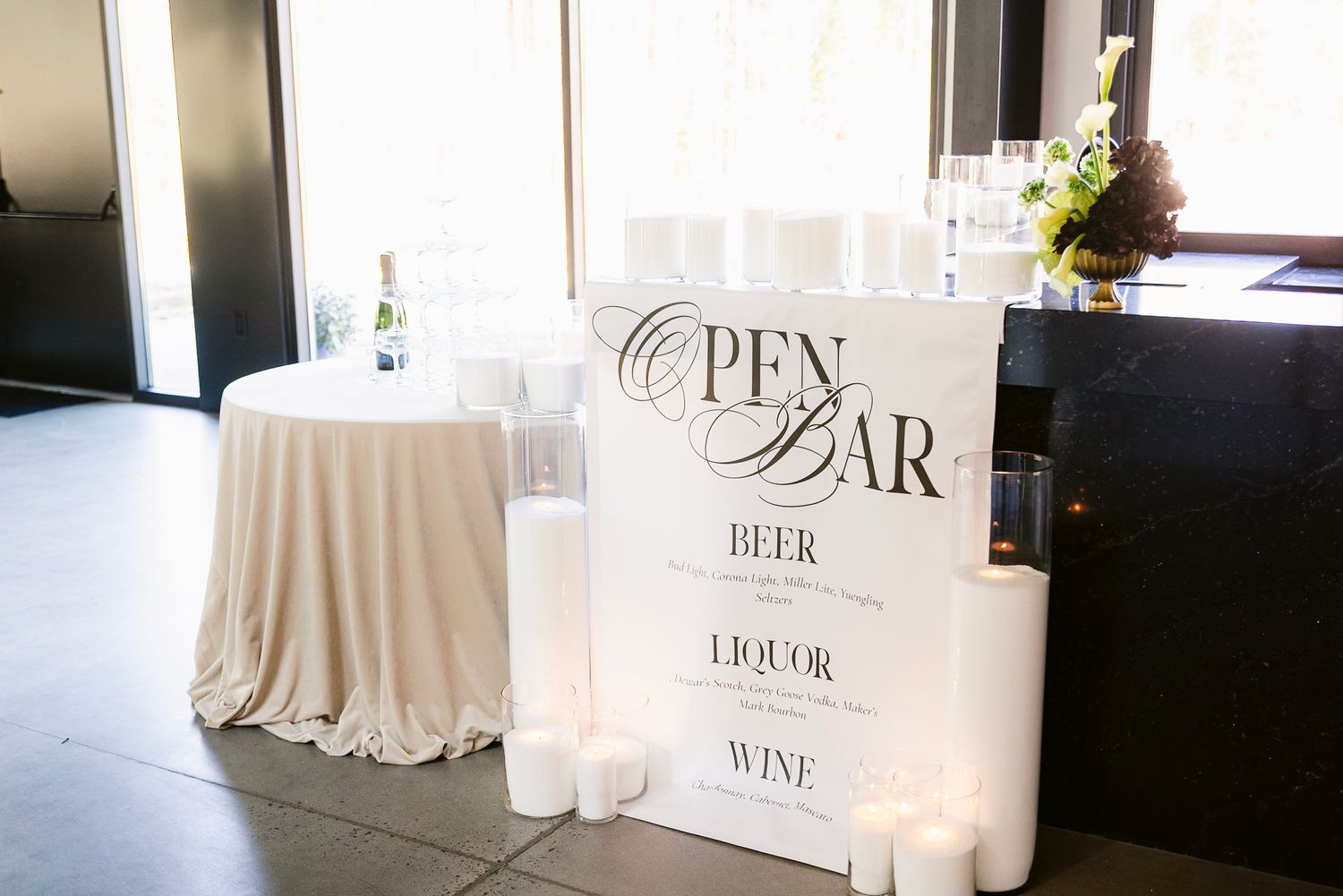 Bar setup at a wedding reception with white tablecloths and signage for beer, wine, and liquor stations.
