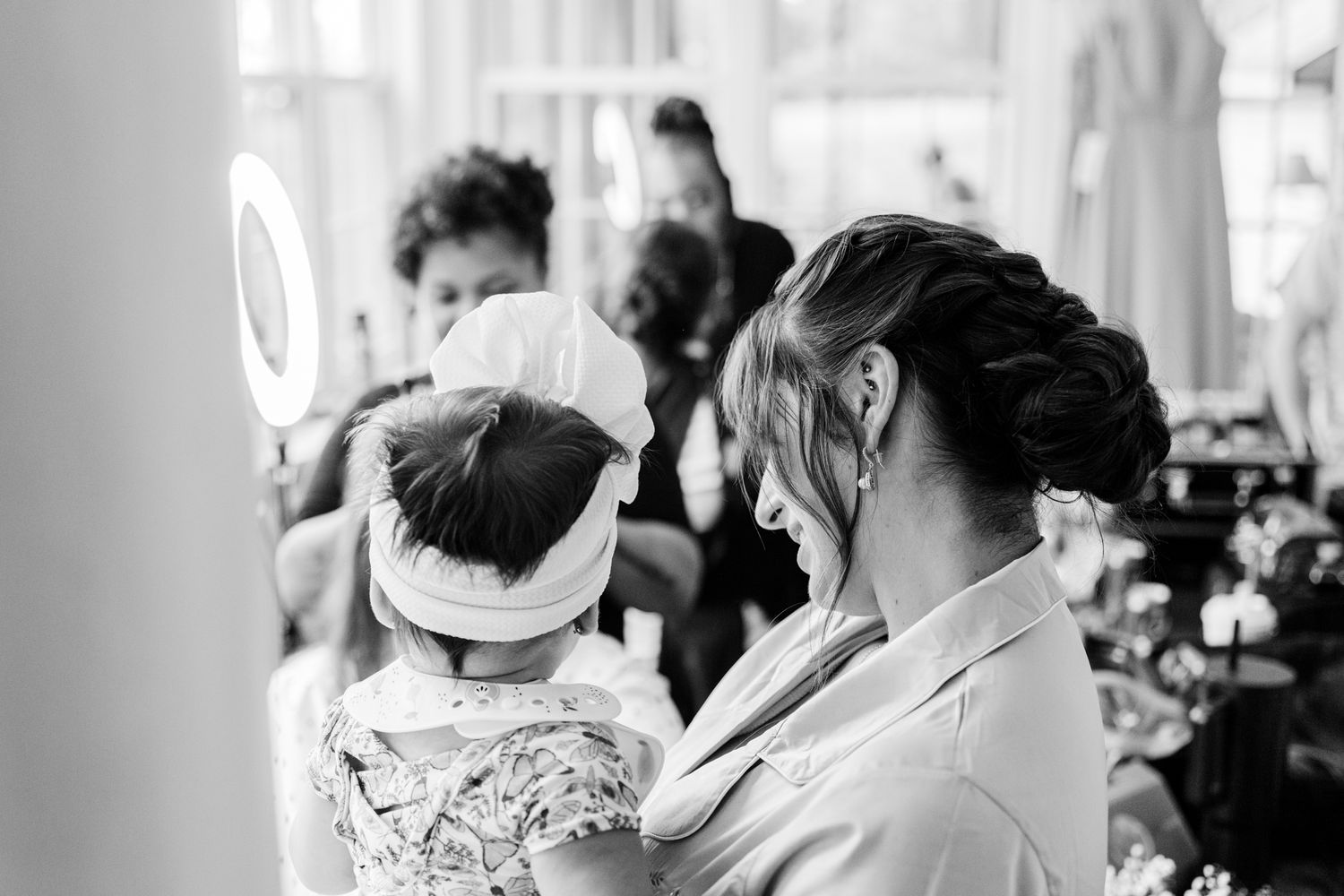 A black and white candid photo shows people at a formal event, with a person wearing a headband in focus.