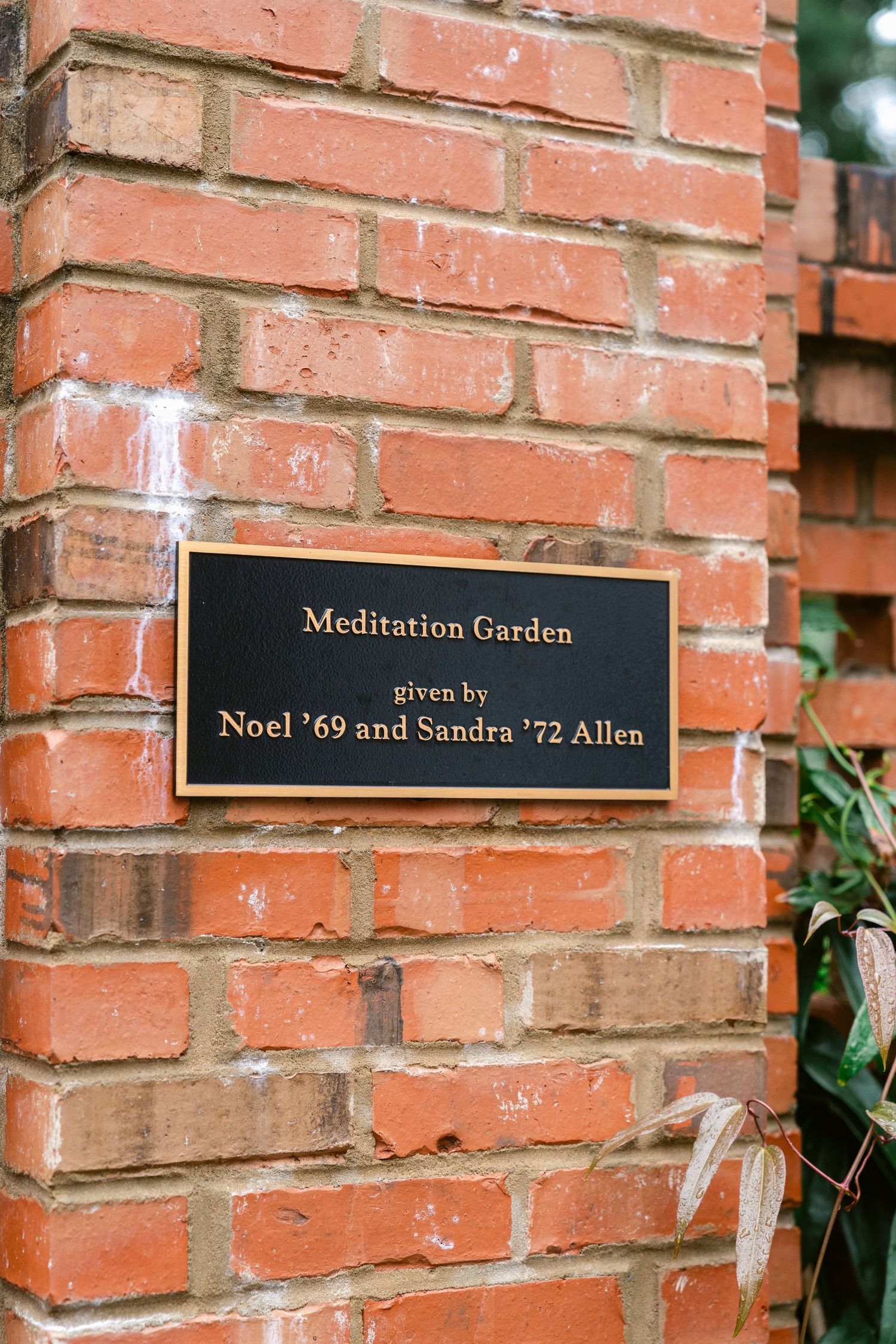 A bronze plaque on red brick wall marks the Meditation Garden given by Noel and Sandra Allen.