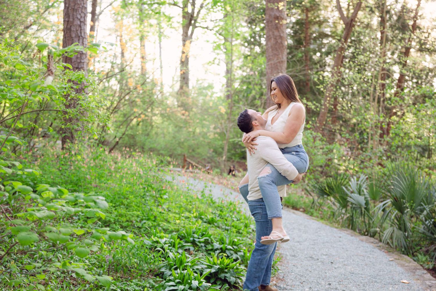 A couple embraces on a sunlit forest path surrounded by lush greenery and trees during a romantic photoshoot.