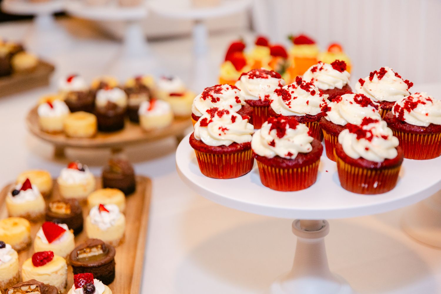 Red velvet cupcakes topped with cream cheese frosting and red sprinkles displayed on white cake stands.