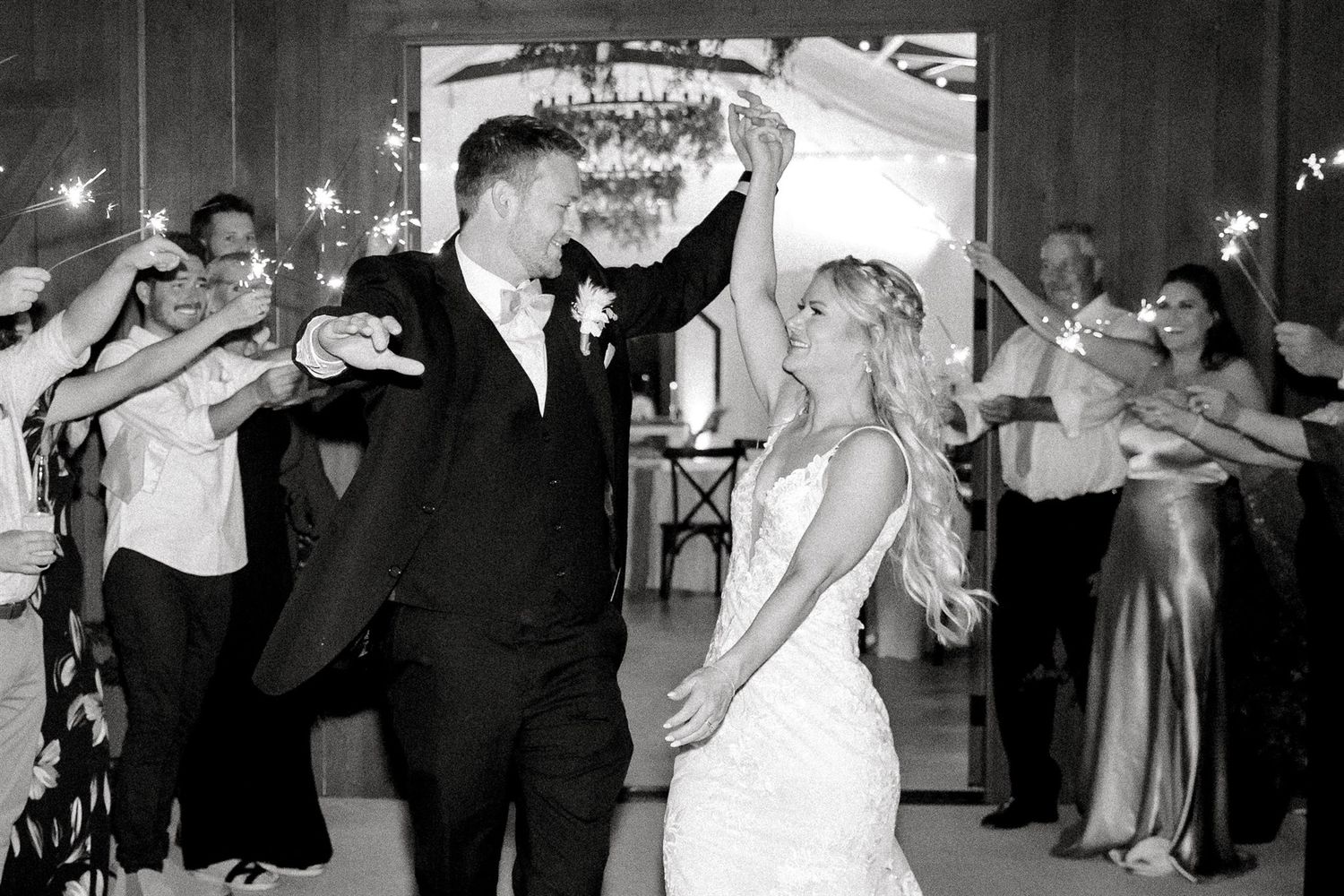 Wedding couple celebrates with guests in a sparkler exit tunnel captured in black and white.