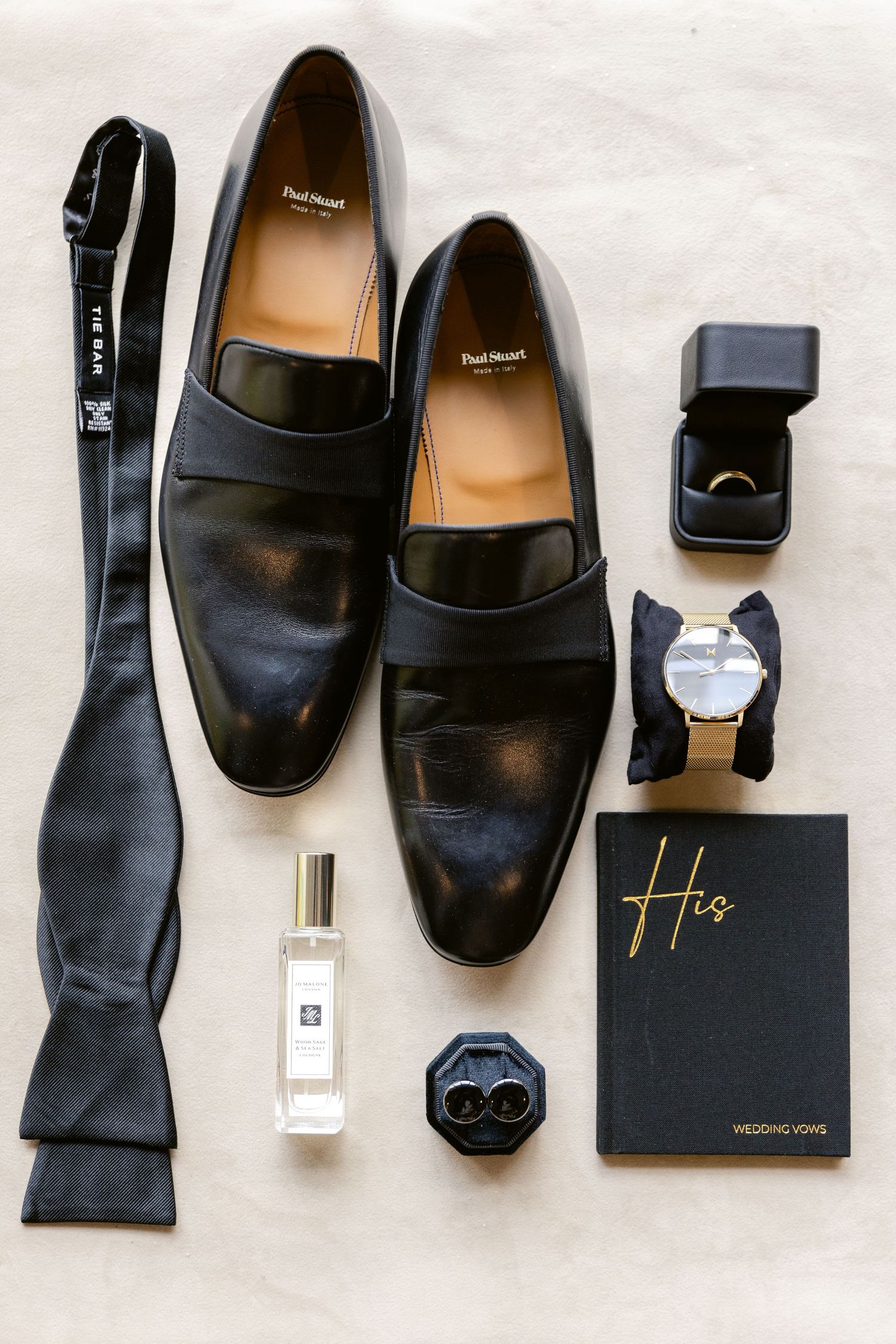 Groom's accessories including black leather shoes, bow tie, watch, ring box and fragrance.