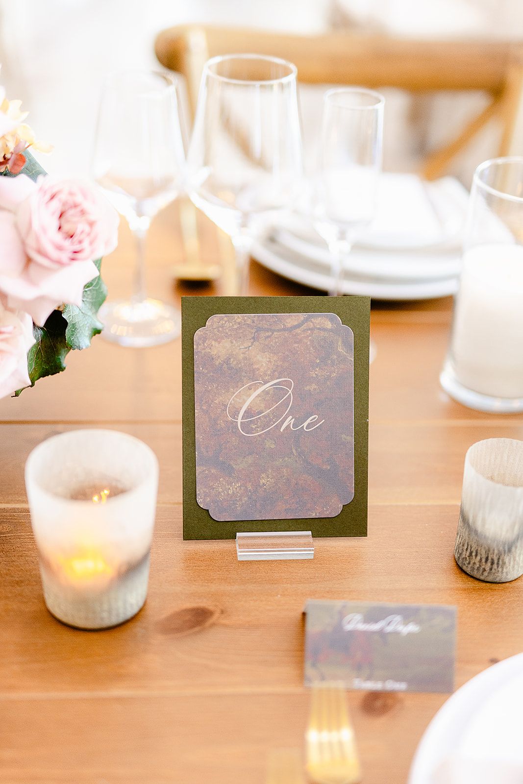 Wedding table details showing place cards, small floral arrangements, and candles on wooden surfaces.