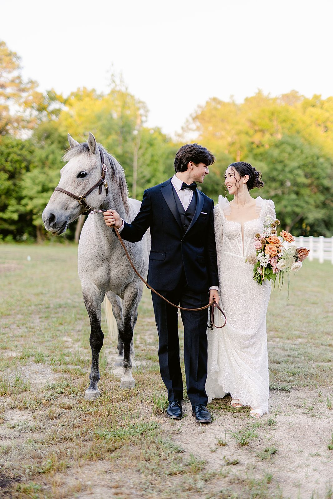 Newlyweds pose with a majestic grey horse in an autumn field during their wedding photoshoot.