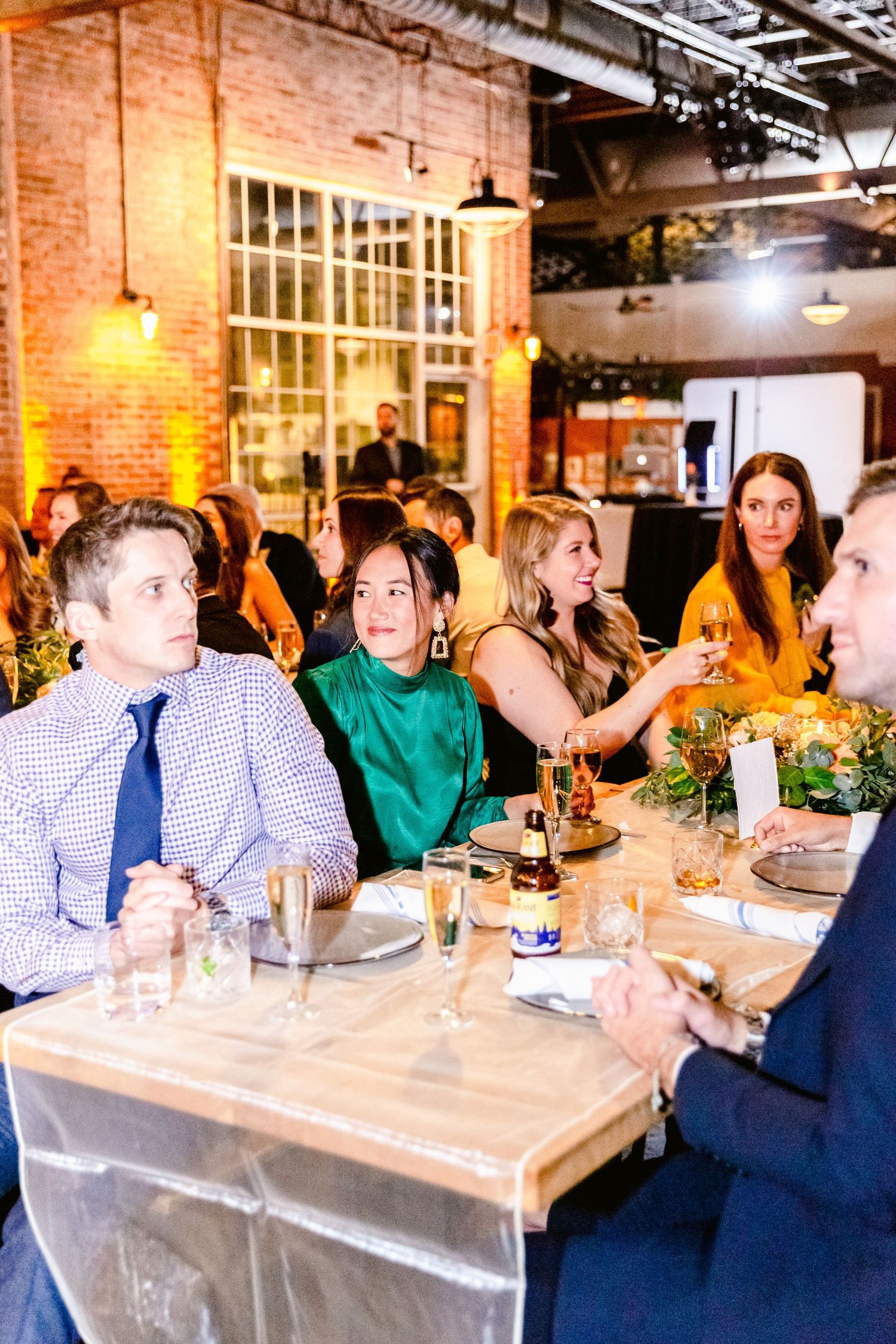 Guests enjoy dinner and conversation at a rustic indoor venue with exposed brick walls and warm lighting.