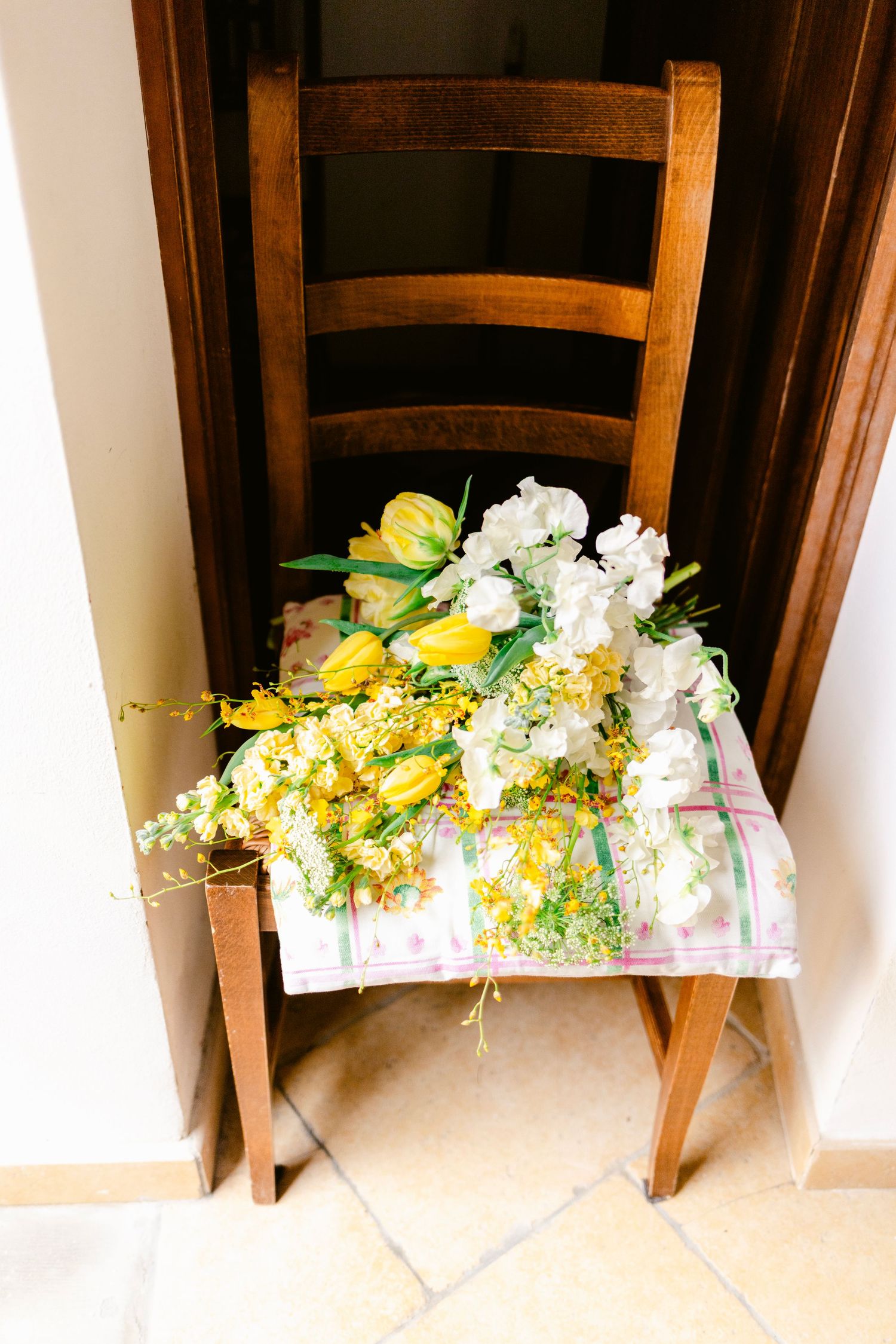A rustic wooden chair adorned with a beautiful bouquet of yellow tulips and white flowers on a floral patterned cloth.