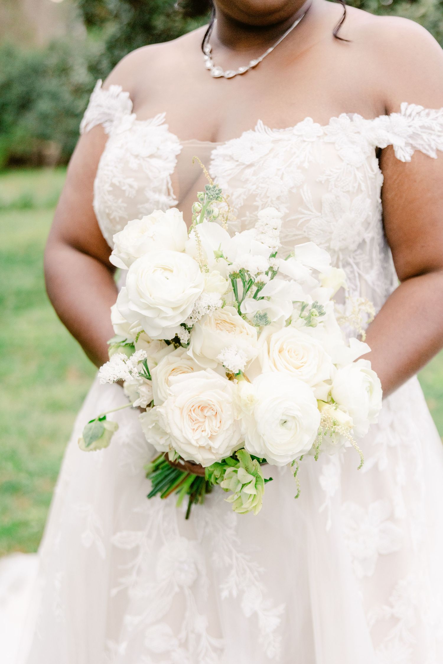 Close-up details of a white wedding bouquet with roses and delicate floral arrangements against a soft outdoor background.