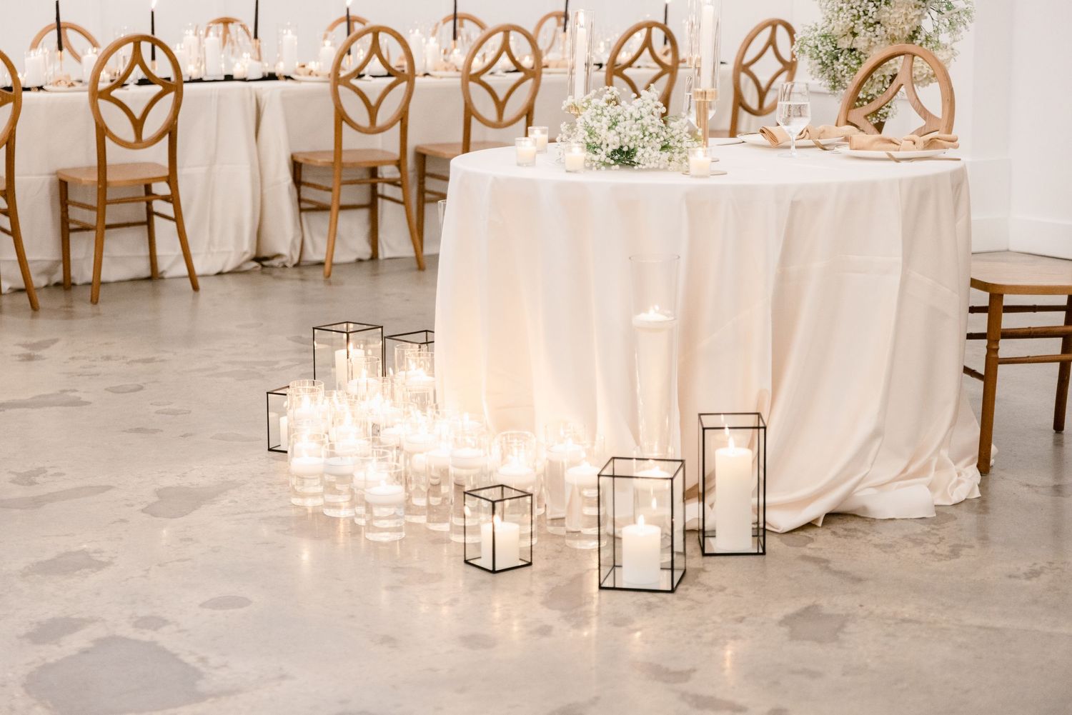 White lanterns with glowing candles line the aisle at an elegant indoor wedding ceremony setup.