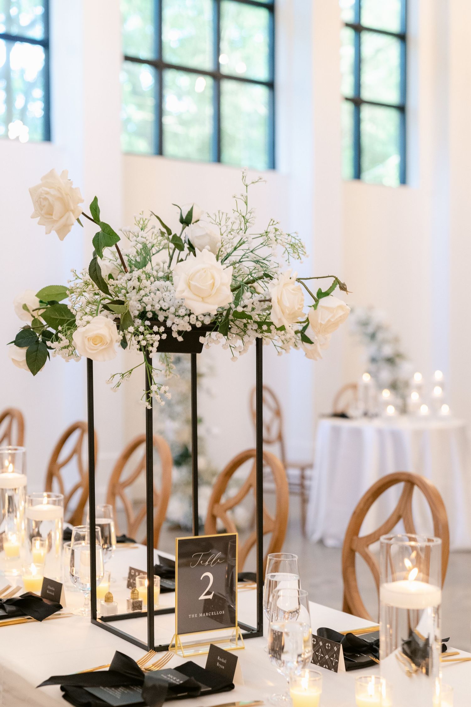 Elegant wedding reception table decor with white lanterns, floral arrangements and table numbers in black frames.